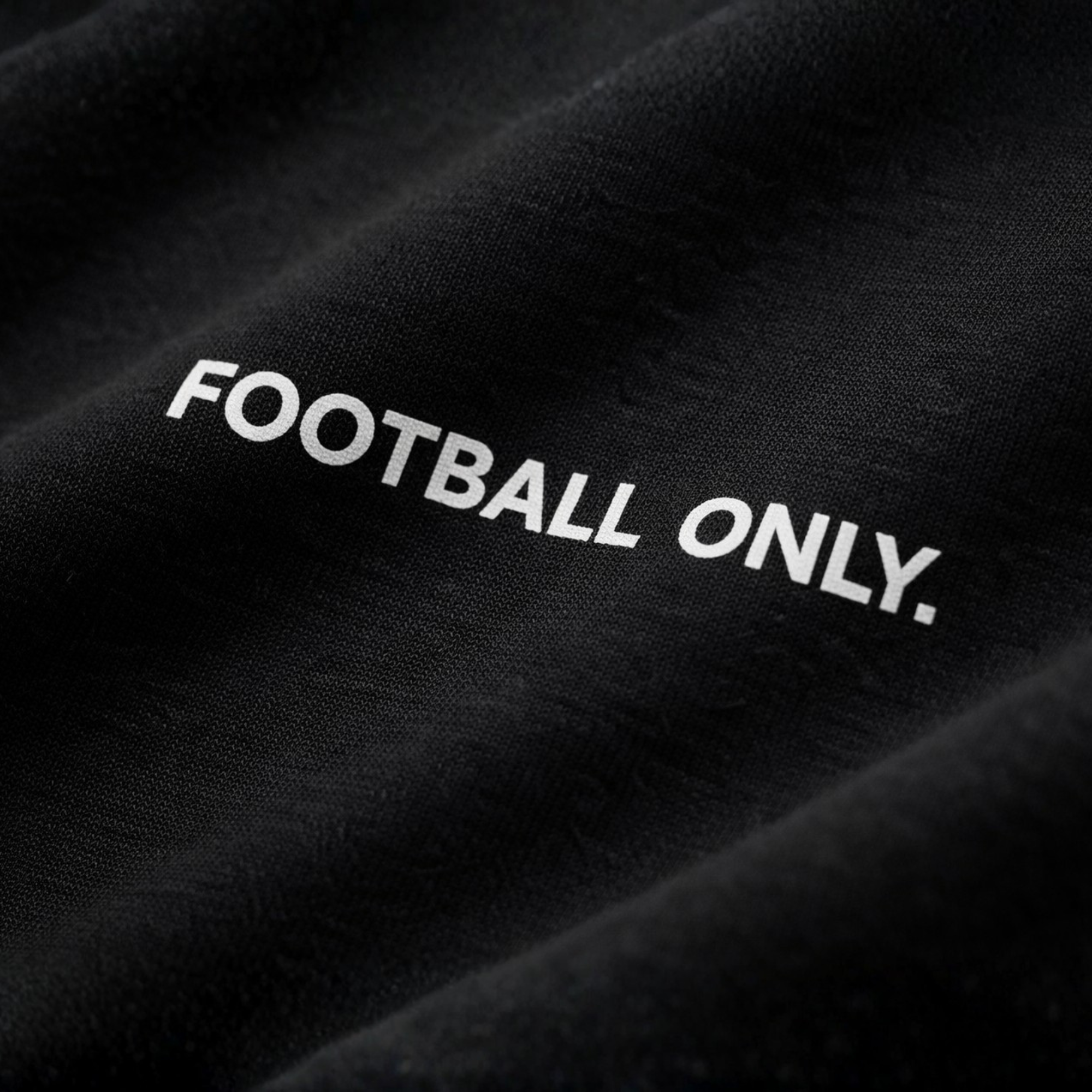 Detailaufnahme eines schwarzen T-Shirts mit weißem „Football Only“ Schriftzug, Fokus auf Stoffstruktur und Druckqualität, dunkler, edler Studio-Look