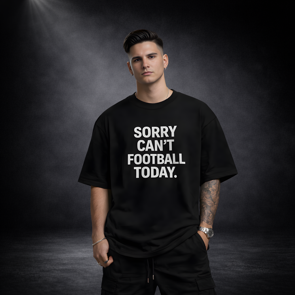 Männliches Model trägt schwarzes Oversized T-Shirt mit großem weißen Schriftzug „Sorry Can’t Football Today“, moderner Streetwear Look auf dunklem Studio-Hintergrund
