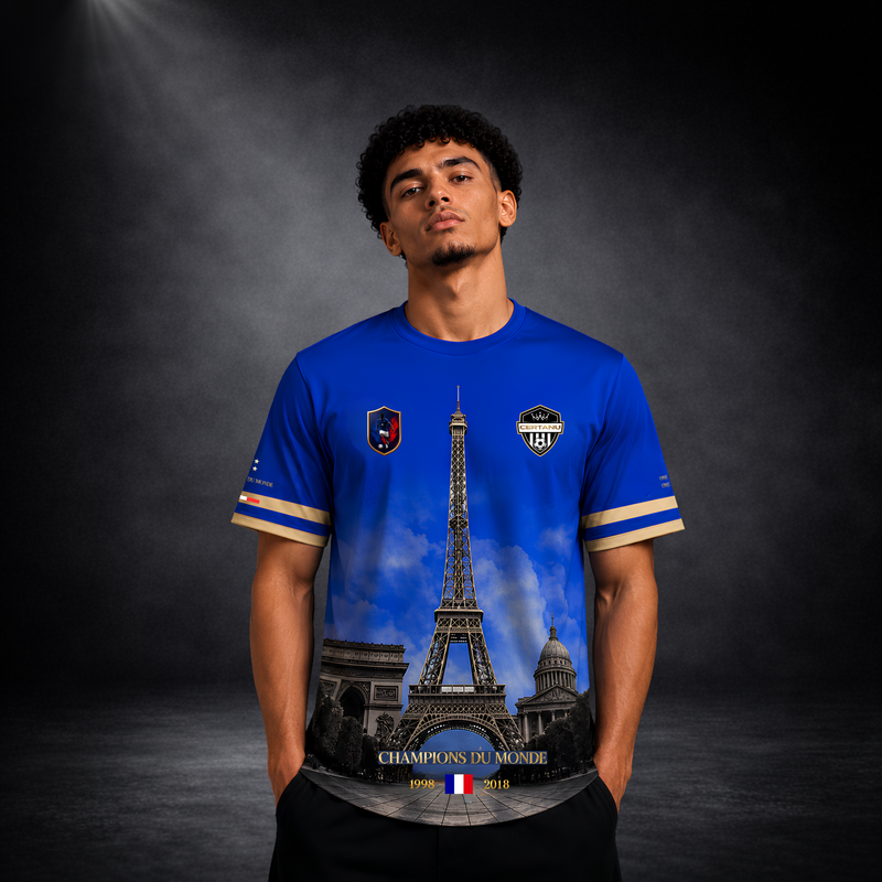 Junger männlicher Fan trägt ein blaues CERTANU Frankreich Premium Fußballshirt vor dunklem Studiohintergrund. Das exklusive Fan-Shirt zeigt den Eiffelturm als zentrales Motiv sowie weitere ikonische Pariser Wahrzeichen in einem hochwertigen Allover-Design. Auf der Brust befinden sich das CERTANU-Wappen und ein Frankreich-Emblem. Goldene Ärmelabschlüsse und edle Details verleihen dem Trikot einen luxuriösen Look. Der Schriftzug „Champions du Monde“ mit den Weltmeisterjahren 1998 und 2018 sowie die französisc