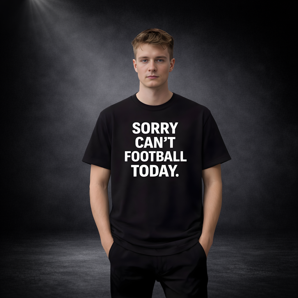 Junger Mann vor dunklem Studio-Hintergrund trägt ein schwarzes T-Shirt mit weißem Aufdruck „SORRY CAN’T FOOTBALL TODAY.“ und steht frontal mit neutralem Gesichtsausdruck
