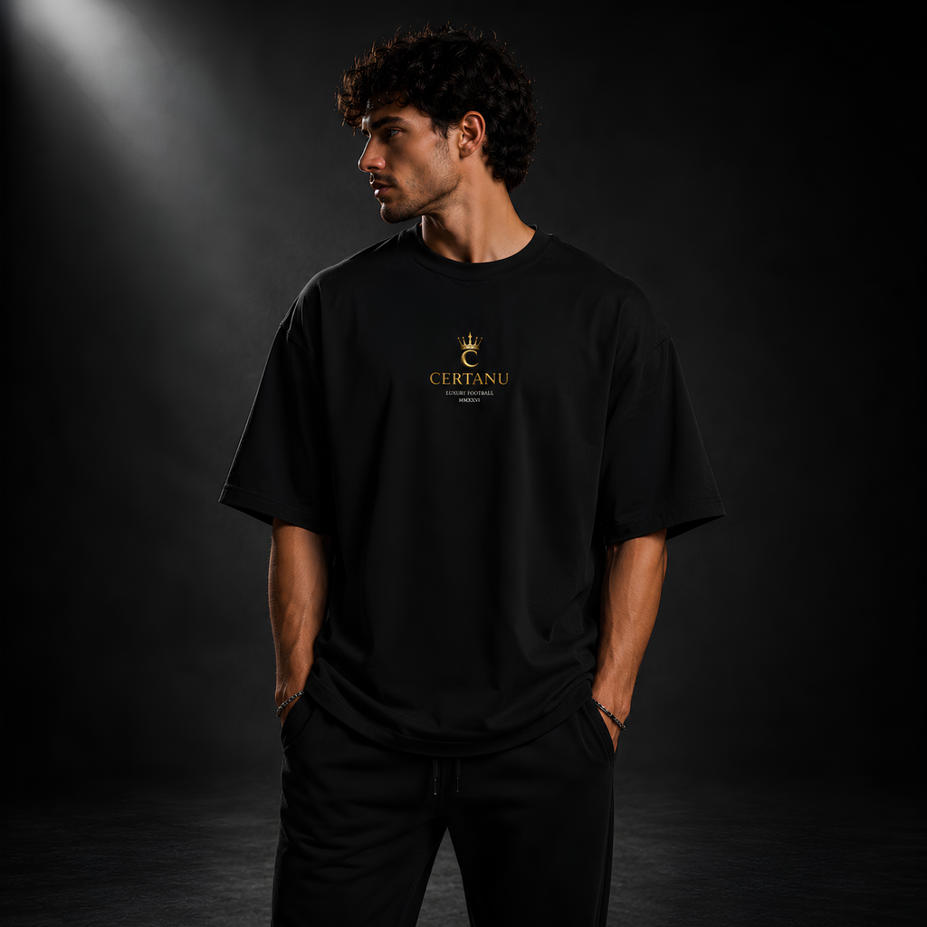 Junger Mann trägt ein schwarzes CERTANU Oversized Premium T-Shirt mit dezentem goldenen Brustlogo. Das minimalistische Design mit Krone und CERTANU-Schriftzug steht für hochwertige Fußball Streetwear, modernen Luxus und zeitlosen Lifestyle. Eleganter Studio-Look mit dunklem Hintergrund, Premium Baumwoll-Shirt für Herren, exklusiver Oversized Fit und hochwertige Fanmode im minimalistischen Stil.
