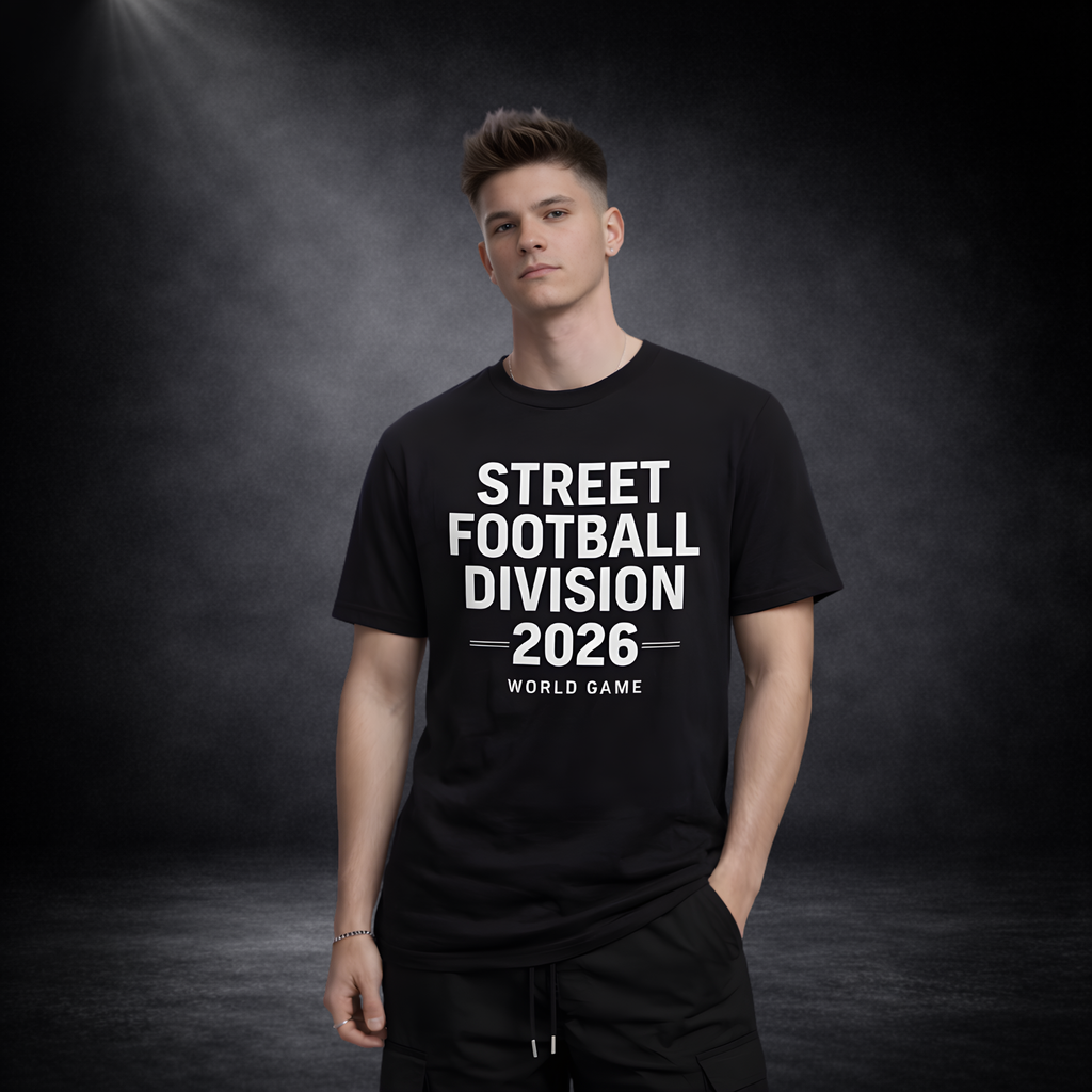 Mann trägt schwarzes T-Shirt mit weißem Schriftzug „STREET FOOTBALL DIVISION 2026 – WORLD GAME“, stehend vor dunklem Studio-Hintergrund mit Spotlight-Effekt