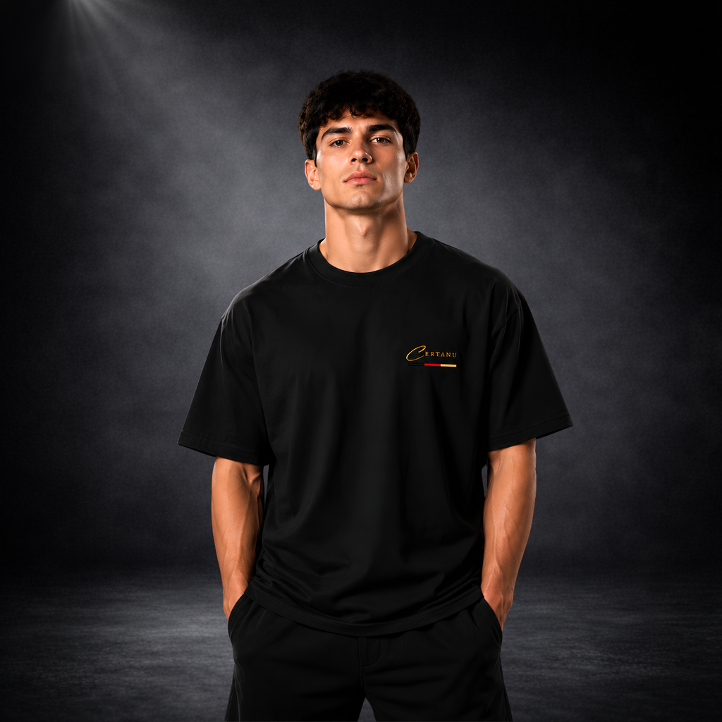 Junger Mann trägt ein schwarzes CERTANU Oversized T-Shirt vor dunklem Studiohintergrund. Das minimalistische Premium-Shirt besitzt ein kleines goldenes CERTANU-Logo auf der linken Brust mit dezentem Akzent in Schwarz, Rot und Gold. Der moderne Oversized-Fit, hochwertige Stoffqualität und das zeitlose Design machen das T-Shirt ideal für Fußballfans, Streetwear, Freizeit und Alltag. Elegantes Lifestyle-Produktbild mit Fokus auf Passform, Komfort und exklusivem CERTANU-Markendesign.