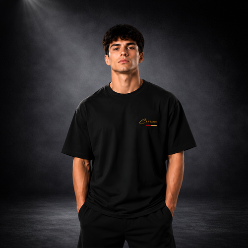 Junger Mann trägt ein schwarzes CERTANU Oversized T-Shirt vor dunklem Studiohintergrund. Das minimalistische Premium-Shirt besitzt ein kleines goldenes CERTANU-Logo auf der linken Brust mit dezentem Akzent in Schwarz, Rot und Gold. Der moderne Oversized-Fit, hochwertige Stoffqualität und das zeitlose Design machen das T-Shirt ideal für Fußballfans, Streetwear, Freizeit und Alltag. Elegantes Lifestyle-Produktbild mit Fokus auf Passform, Komfort und exklusivem CERTANU-Markendesign.
