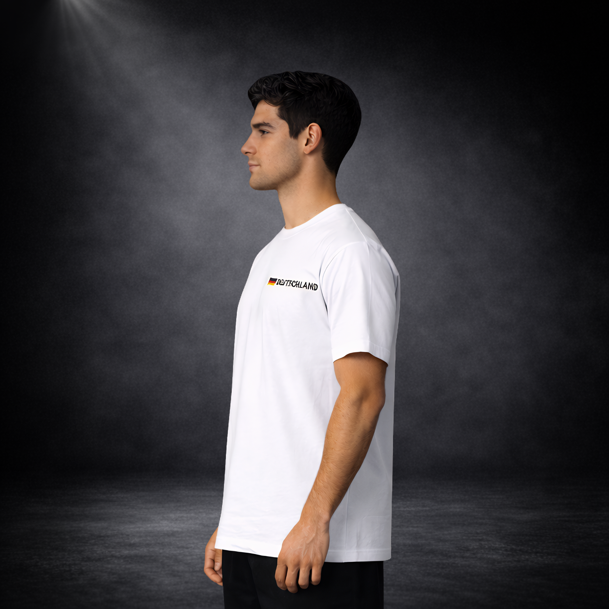 Seitenansicht eines Mannes im weißen Deutschland Fan T-Shirt mit kleinem Flaggen-Detail und „Deutschland“-Schriftzug auf der Brust, minimalistischer Fußball WM 2026 Look vor dunklem Studio Hintergrund
