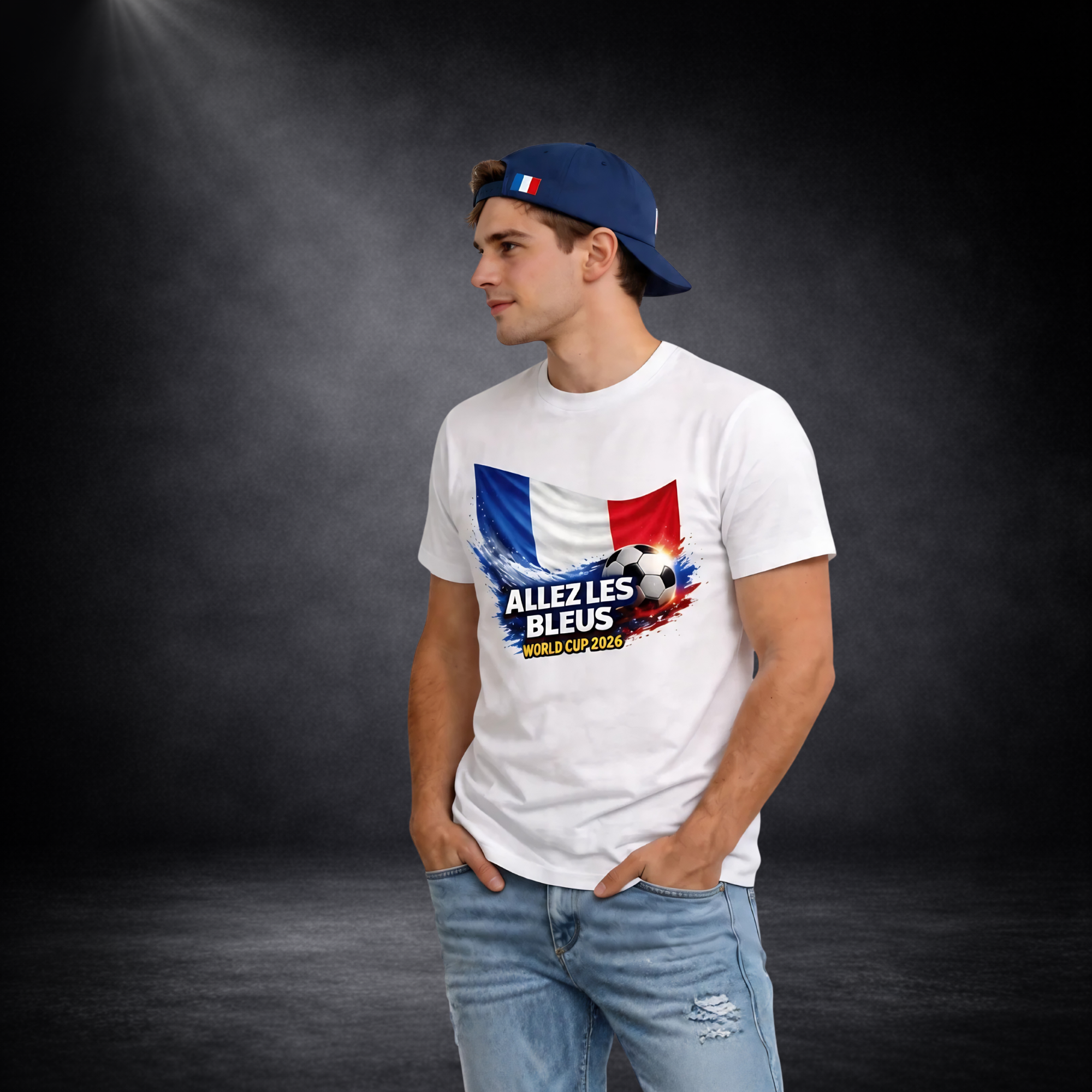 Junger Mann im Seitenprofil trägt ein weißes T-Shirt mit Frankreich-Flagge, Fußballmotiv und „ALLEZ LES BLEUS – WORLD CUP 2026“, kombiniert mit Jeans und rückwärts getragener Cap, vor dunklem Studio-Hintergrund