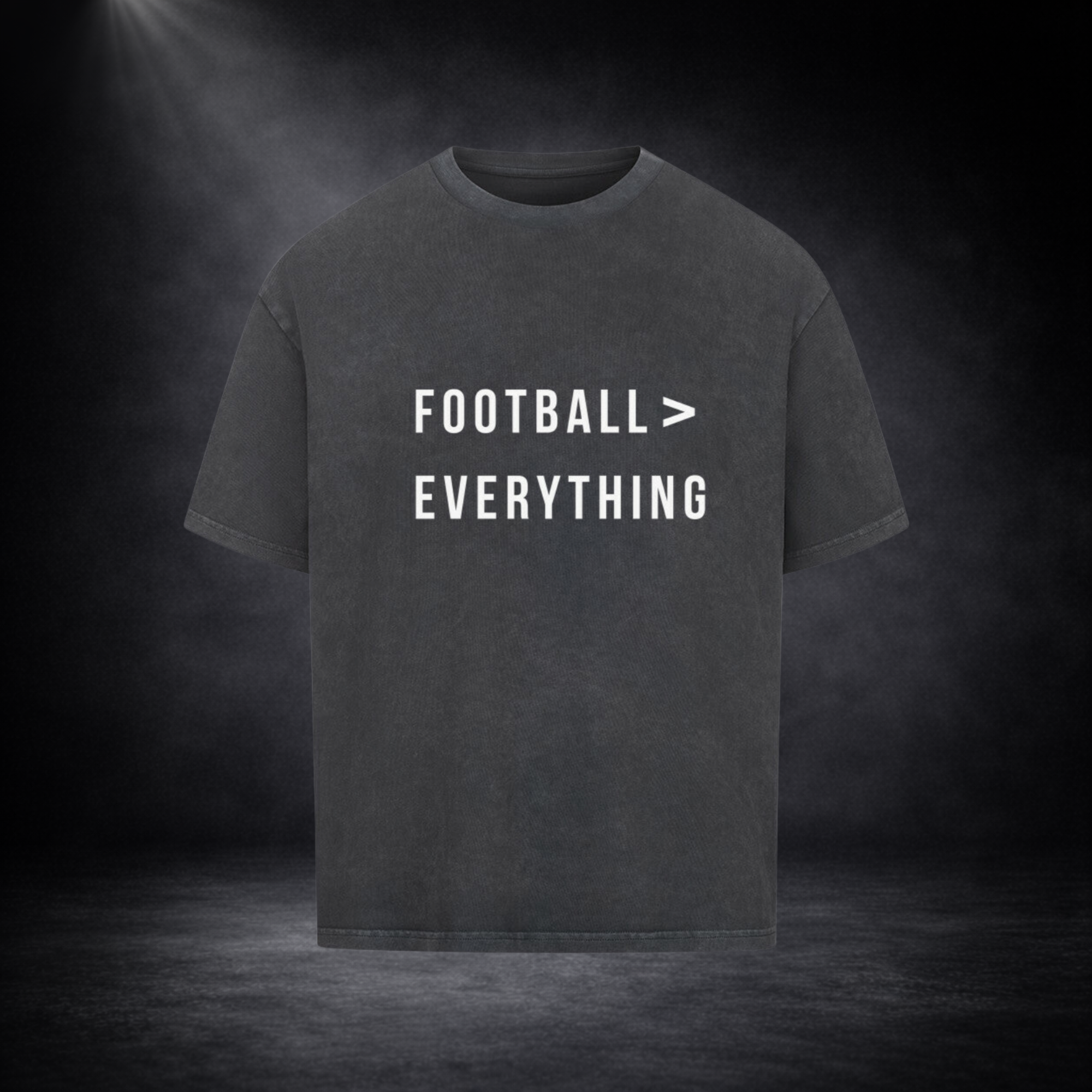 Dunkelgraues Oversized T-Shirt mit weißem Schriftzug „Football > Everything“ auf der Vorderseite, freigestellt vor dunklem Studio-Hintergrund mit Spotlight und dezenter Nebelwirkung