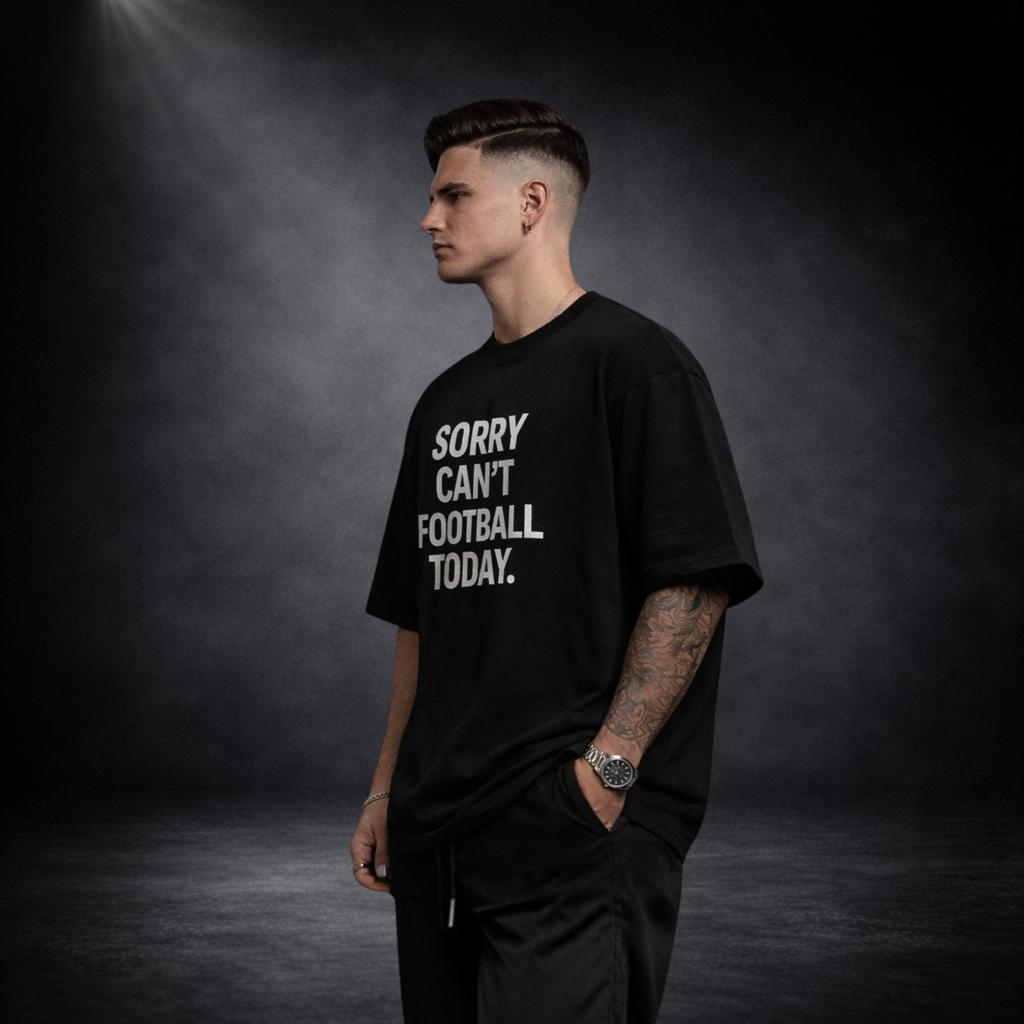 Seitliche Ansicht eines männlichen Models mit schwarzem Oversized T-Shirt und weißem „Sorry Can’t Football Today“ Print, moderner Streetwear Look vor dunklem Studio-Hintergrund