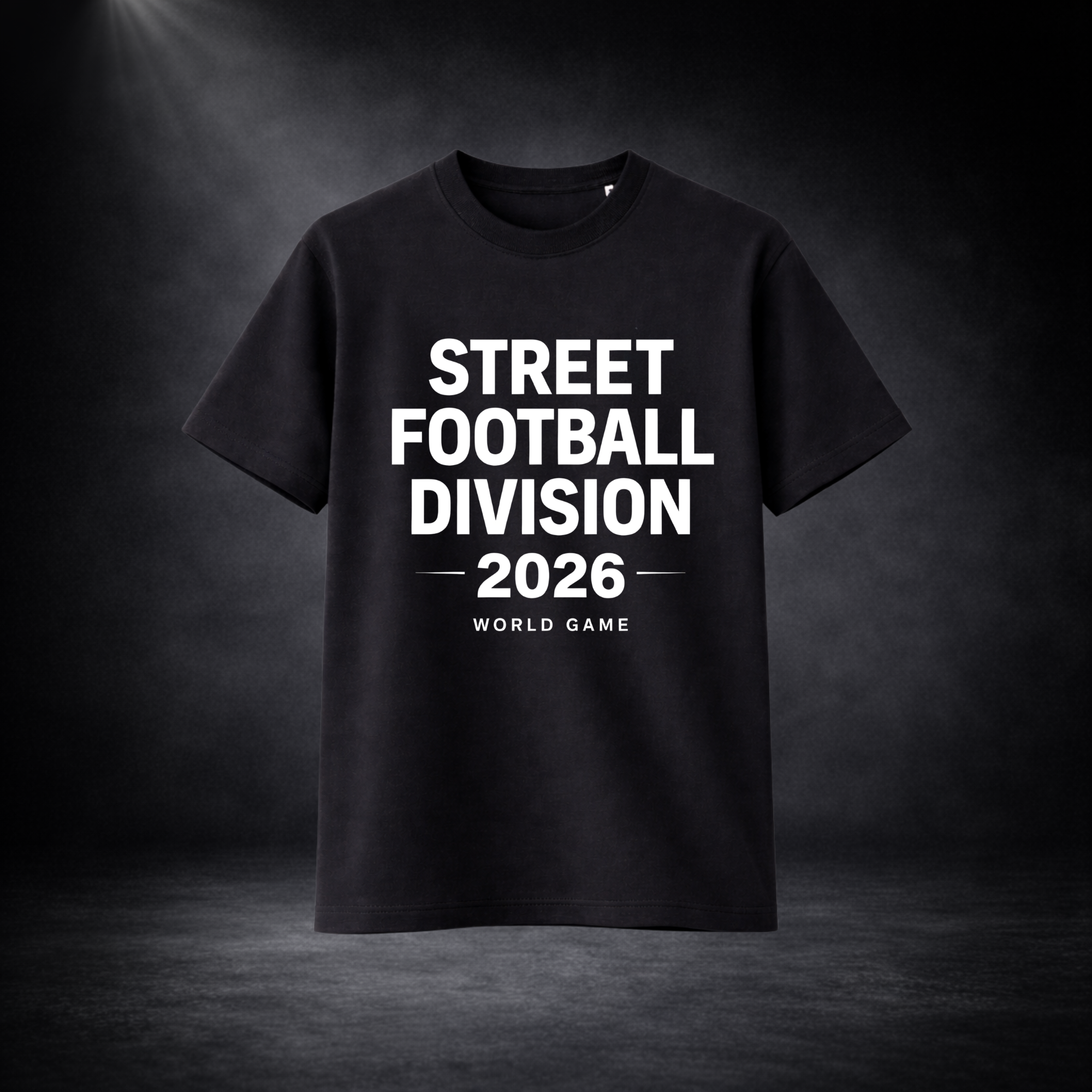 Schwarzes T-Shirt mit weißem Schriftzug „STREET FOOTBALL DIVISION 2026 – WORLD GAME“, freigestellt vor dunklem Studio-Hintergrund mit Spotlight, zentrierte Produktdarstellung