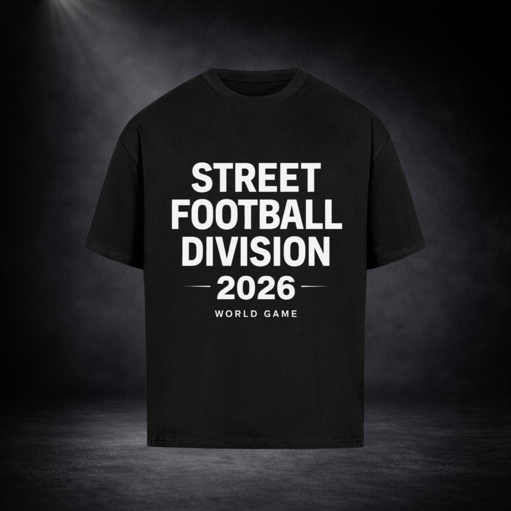 Schwarzes Oversized T-Shirt mit großem weißen Schriftzug „STREET FOOTBALL DIVISION 2026 – WORLD GAME“ auf der Vorderseite, dargestellt vor dunklem Studio-Hintergrund mit Spotlight-Beleuchtung