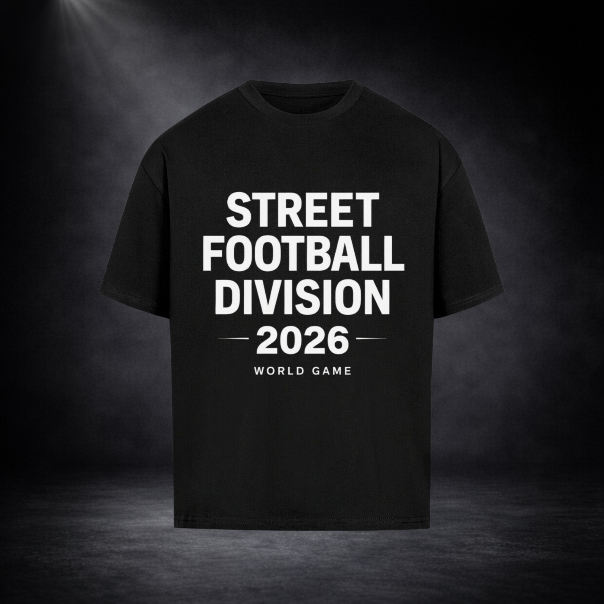 Schwarzes Oversized T-Shirt mit großem weißen Schriftzug „STREET FOOTBALL DIVISION 2026 – WORLD GAME“ auf der Vorderseite, dargestellt vor dunklem Studio-Hintergrund mit Spotlight-Beleuchtung