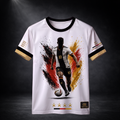 Frontansicht eines weißen CERTANU Deutschland Premium Fußballshirts vor dunklem Studiohintergrund. Das exklusive Design zeigt einen dynamischen Fußballspieler mit der Rückennummer 10 beim Dribbling vor einem kraftvollen Farbsplash in Schwarz, Rot und Gold – den Farben der deutschen Flagge. Vier goldene Sterne symbolisieren die vier Weltmeistertitel Deutschlands. Gold-schwarze Ärmelabschlüsse, historische Weltmeisterjahre (1954, 1974, 1990, 2014) sowie dezente CERTANU-Details verleihen dem Trikot einen hochw