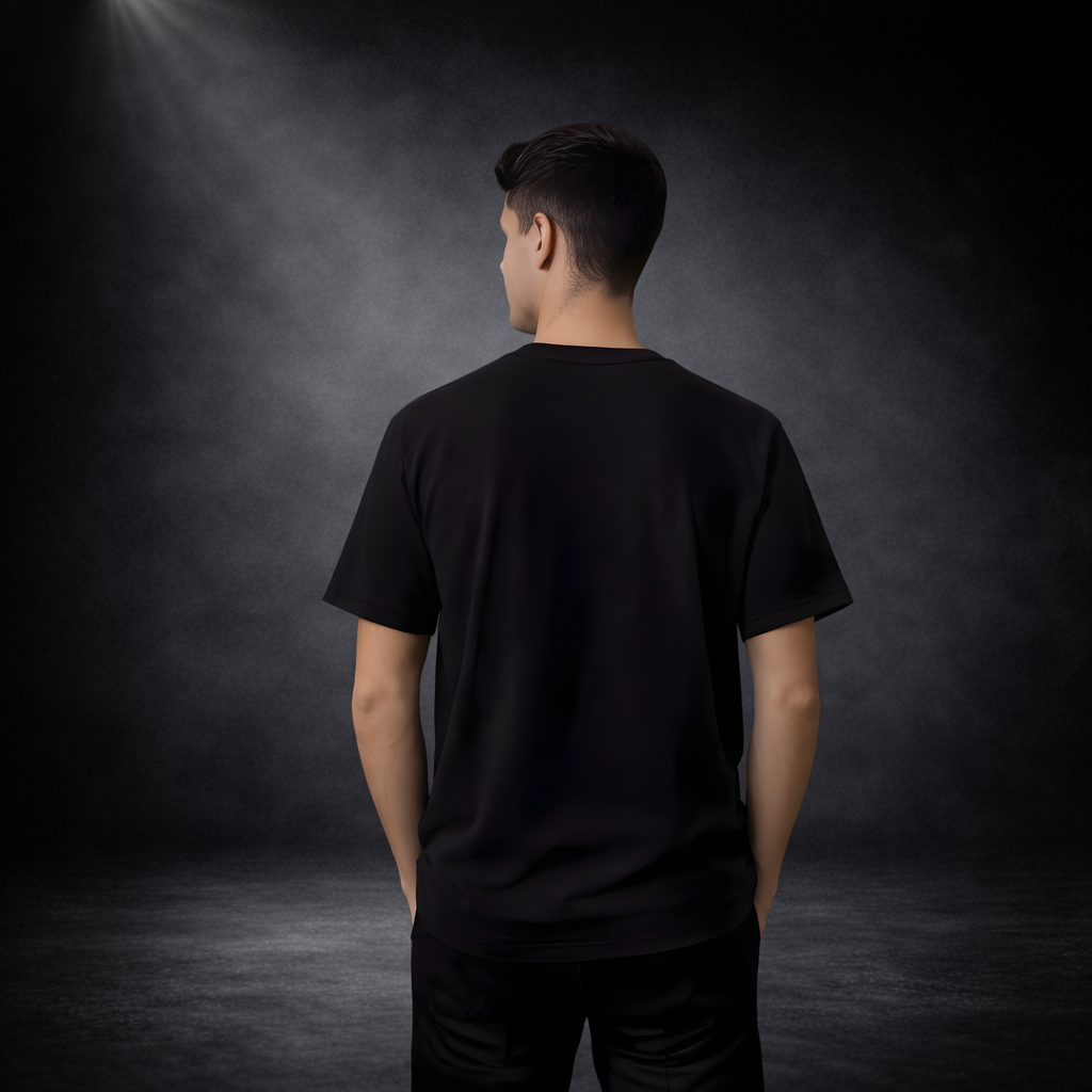 Männliches Model von hinten vor dunklem Studio-Hintergrund, trägt schwarzes T-Shirt ohne Aufdruck, entspannte Haltung mit Händen in den Taschen