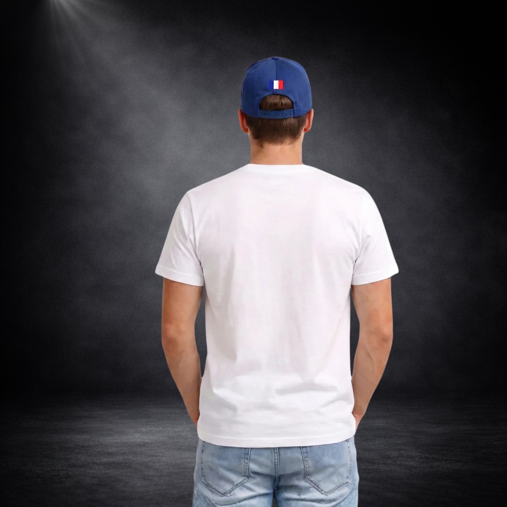 Rückansicht eines jungen Mannes mit weißem T-Shirt ohne Aufdruck, kombiniert mit Jeans und blauer Cap mit kleiner Frankreich-Flagge, vor dunklem Studio-Hintergrund