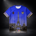 Freigestellte Vorderansicht eines blauen CERTANU Frankreich Premium Fußballshirts vor dunklem Studiohintergrund. Das exklusive Design zeigt den Eiffelturm als zentrales Motiv sowie den Arc de Triomphe und das Panthéon im hochwertigen Allover-Stil. Auf der Brust befinden sich das CERTANU-Wappen und ein Frankreich-Emblem. Goldene Akzente an den Ärmeln sowie der Schriftzug „Champions du Monde“ mit den Weltmeisterjahren 1998 und 2018 unterstreichen die französische Fußballtradition. Das elegante Fan-Shirt verbi