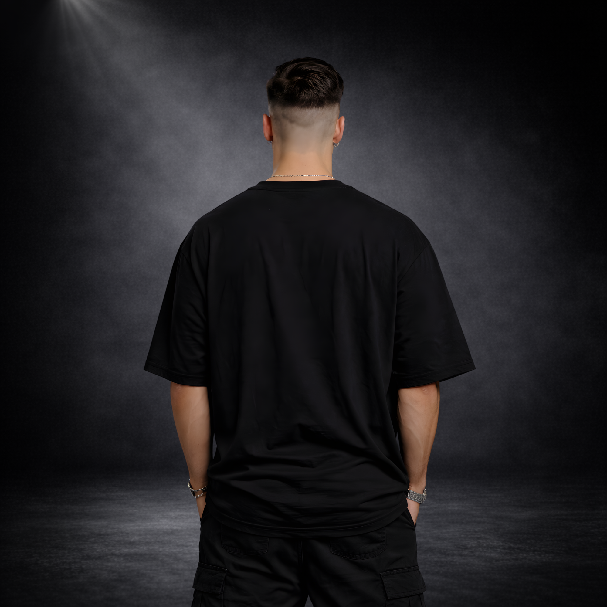 Rückansicht eines männlichen Models mit schwarzem Oversized T-Shirt ohne Print, lockere Passform, minimalistischer Streetwear Look vor dunklem Studio-Hintergrund