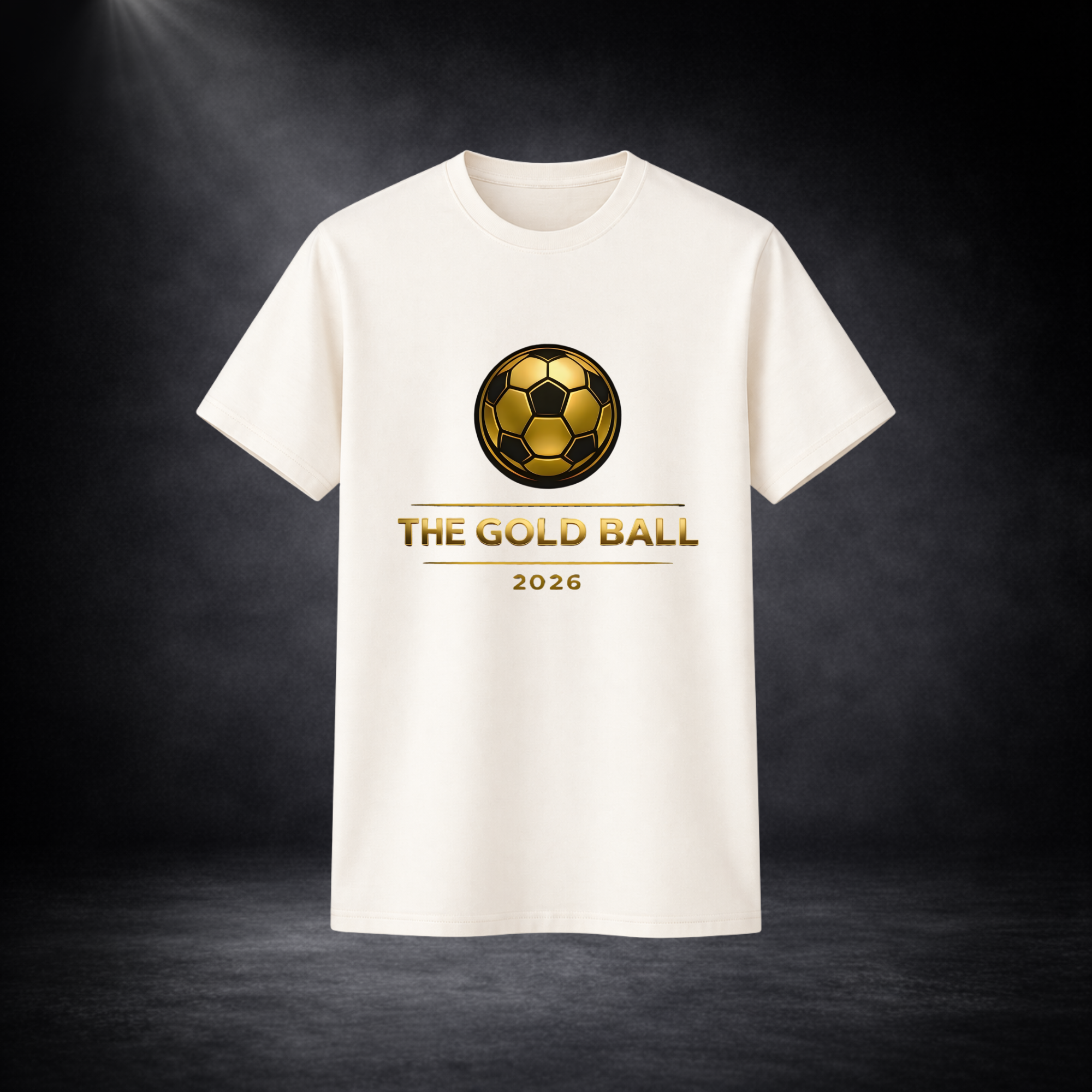 Beige T-Shirt mit goldenem Fußball-Logo und Schriftzug „THE GOLD BALL 2026“ auf der Vorderseite, freigestellt vor dunklem Studio-Hintergrund mit Spotlight von oben links