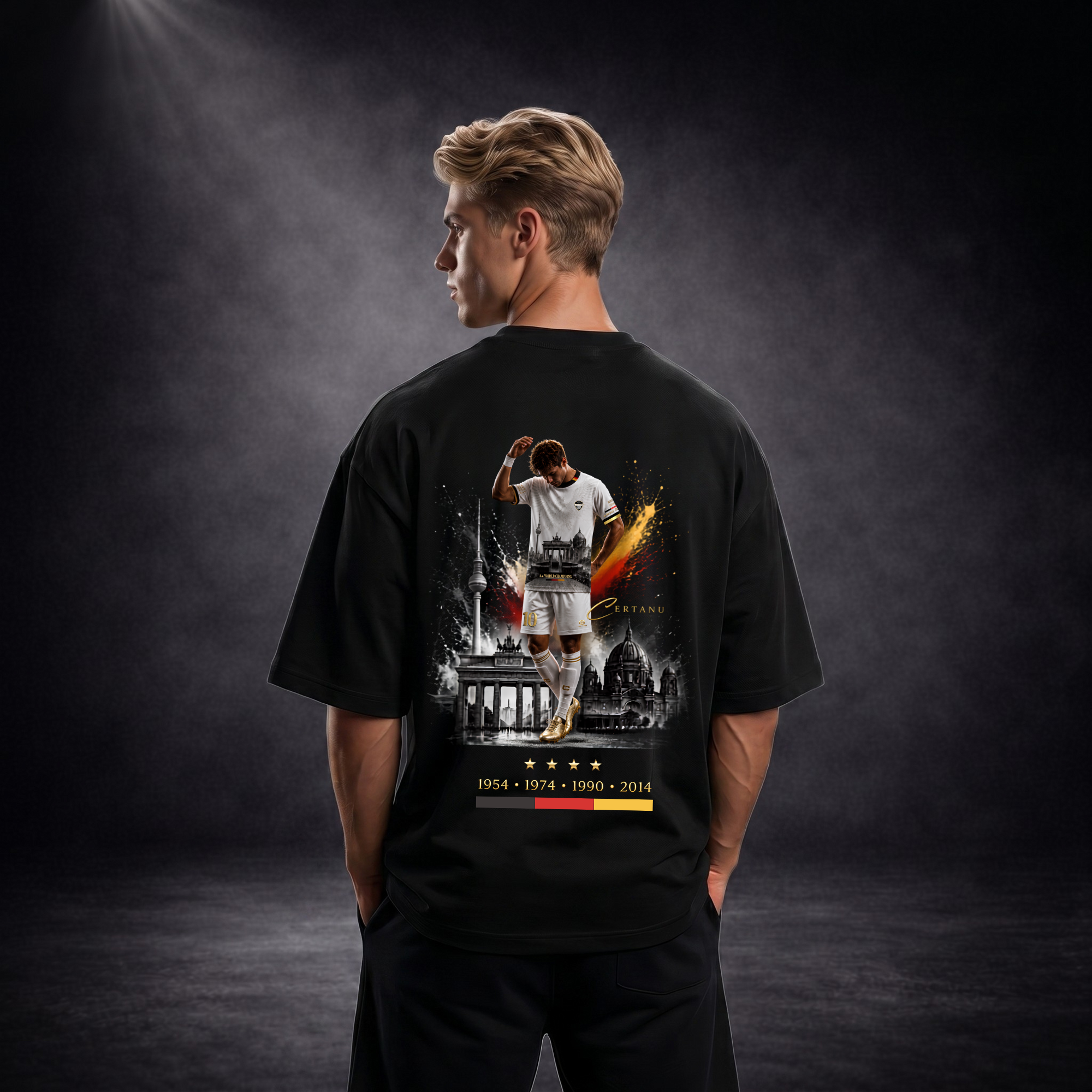 Rückansicht eines jungen blonden Mannes mit schwarzem Oversized CERTANU T-Shirt vor dunklem Studiohintergrund mit Premium-Beleuchtung. Das großflächige Rückendesign zeigt einen Fußballspieler in weißem Trikot vor einer Berlin-Silhouette mit dem Brandenburger Tor, dem Berliner Fernsehturm und dem Berliner Dom. Goldene, rote und schwarze Farbakzente symbolisieren Deutschland und verleihen dem Motiv einen hochwertigen Streetwear-Look. Unter dem Design befinden sich vier goldene Sterne sowie die Jahreszahlen 19