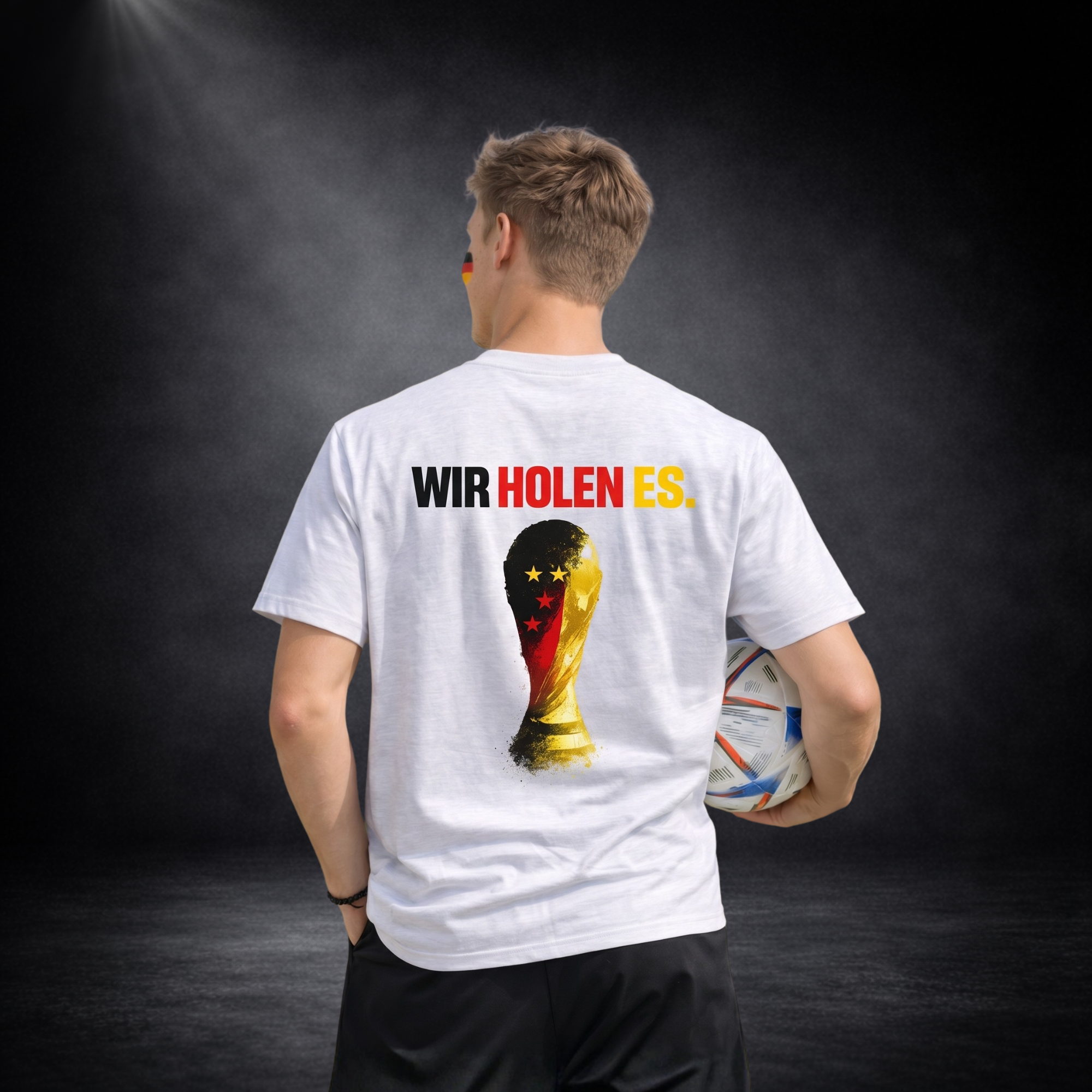 Rückansicht eines Deutschland Fußball Fans mit weißem T-Shirt, großem Backprint „Wir holen es.“ und WM Pokal Motiv in Deutschlandfarben, hält Fußball, WM 2026 Fan Outfit auf dunklem Studio Hintergrund
