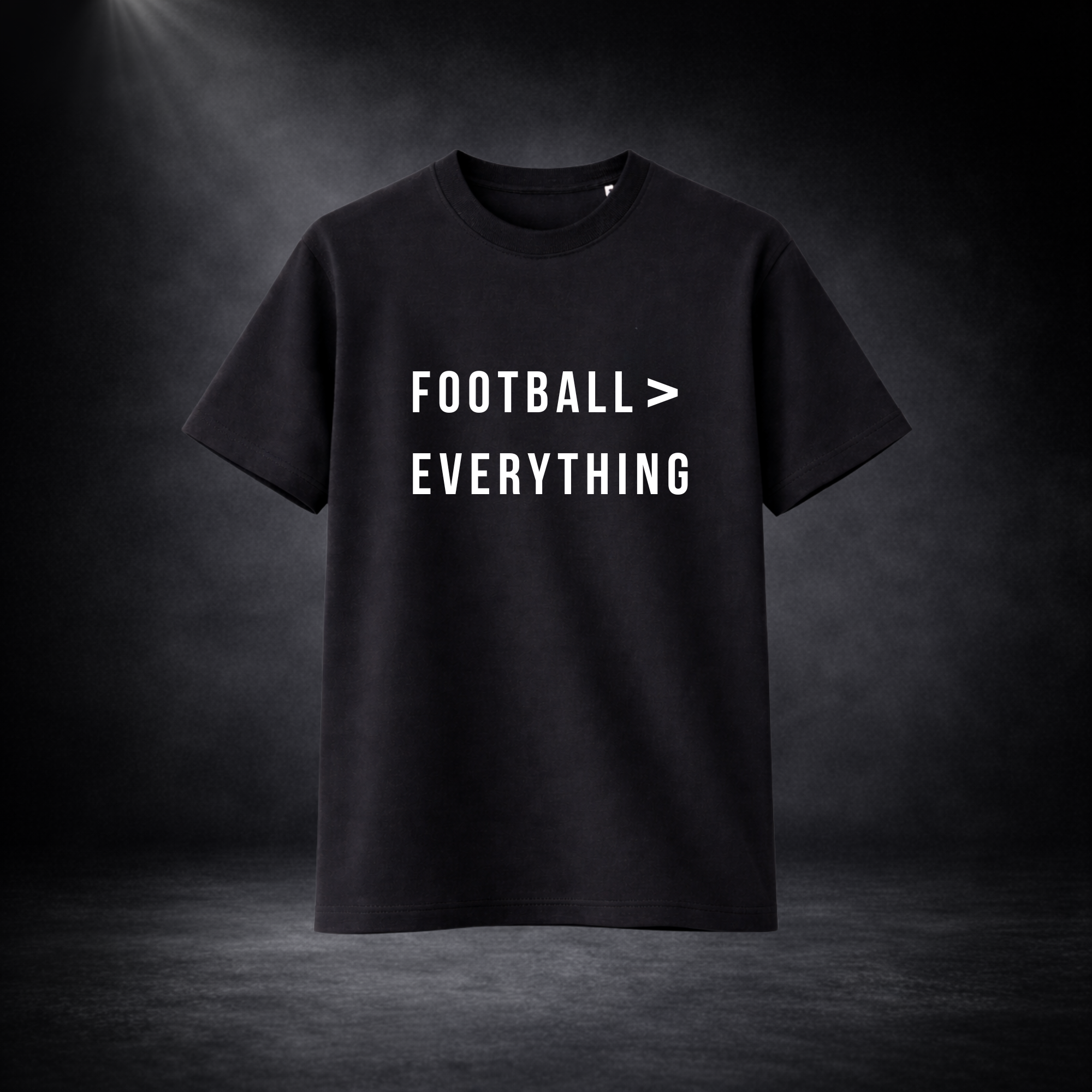 Schwarzes T-Shirt vor dunklem Studio-Hintergrund, frontal dargestellt, mit weißem Aufdruck „FOOTBALL > EVERYTHING“ in klarer, moderner Schrift