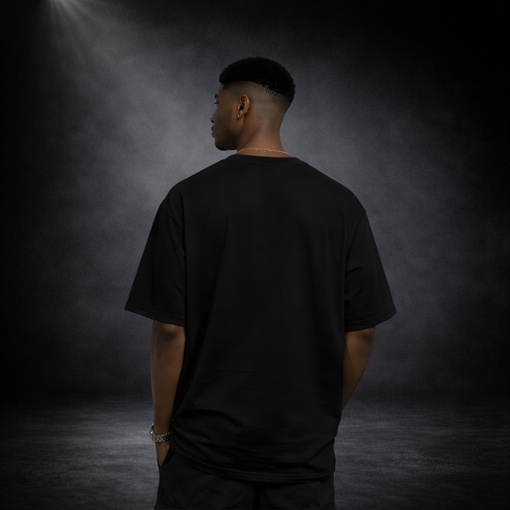 Rückansicht eines männlichen Models in schwarzem Oversized T-Shirt ohne Aufdruck, vor dunklem Studio-Hintergrund mit weichem Licht, Fokus auf Passform und Stofffall