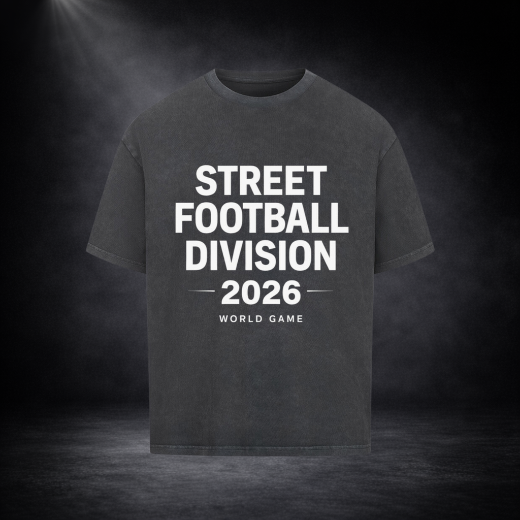 Dunkelgraues Oversized T-Shirt mit weißem Schriftzug „Street Football Division 2026 – World Game“ auf der Vorderseite, präsentiert vor einem dunklen Studio-Hintergrund mit Spotlight-Beleuchtung