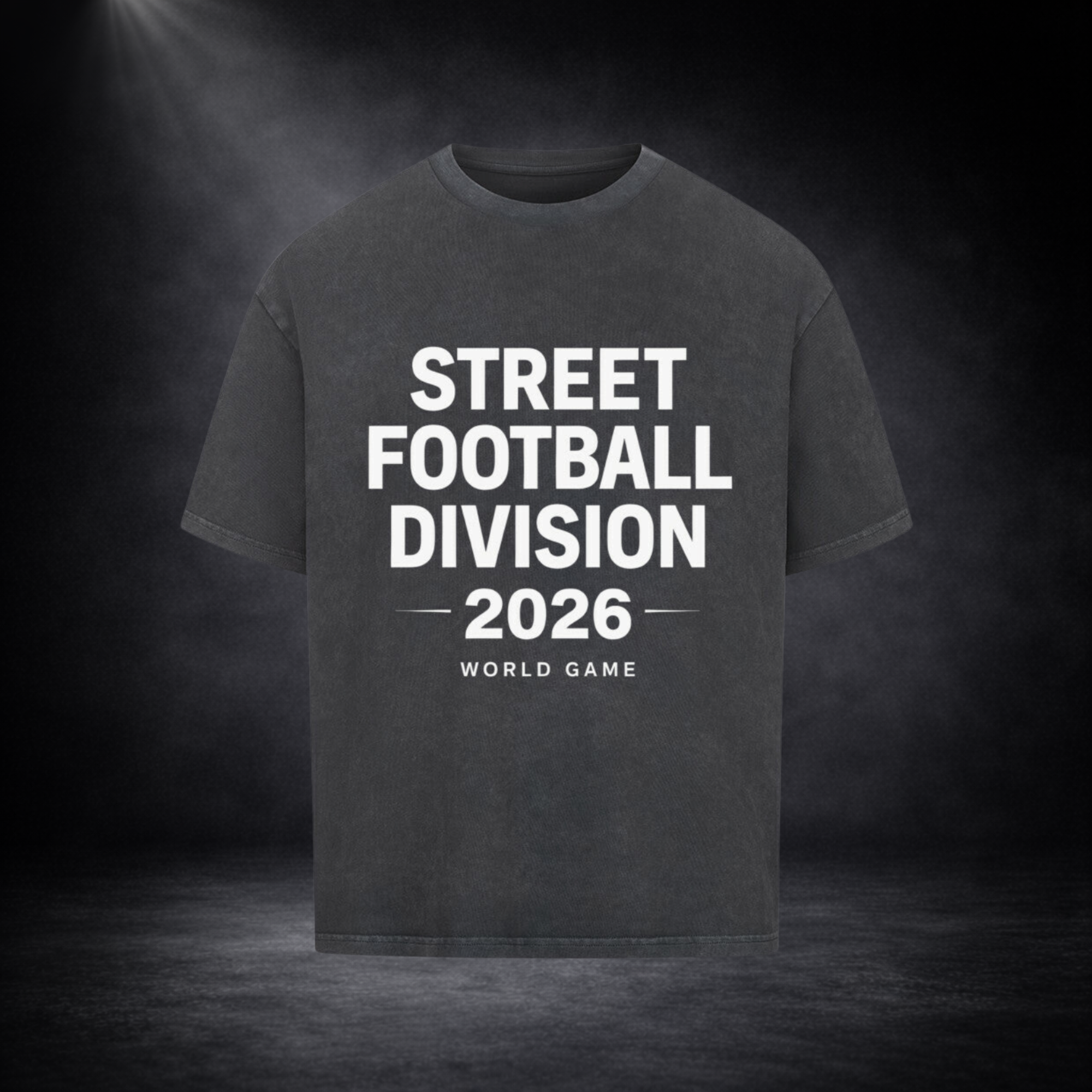 Dunkelgraues Oversized T-Shirt mit weißem Schriftzug „Street Football Division 2026 – World Game“ auf der Vorderseite, präsentiert vor einem dunklen Studio-Hintergrund mit Spotlight-Beleuchtung