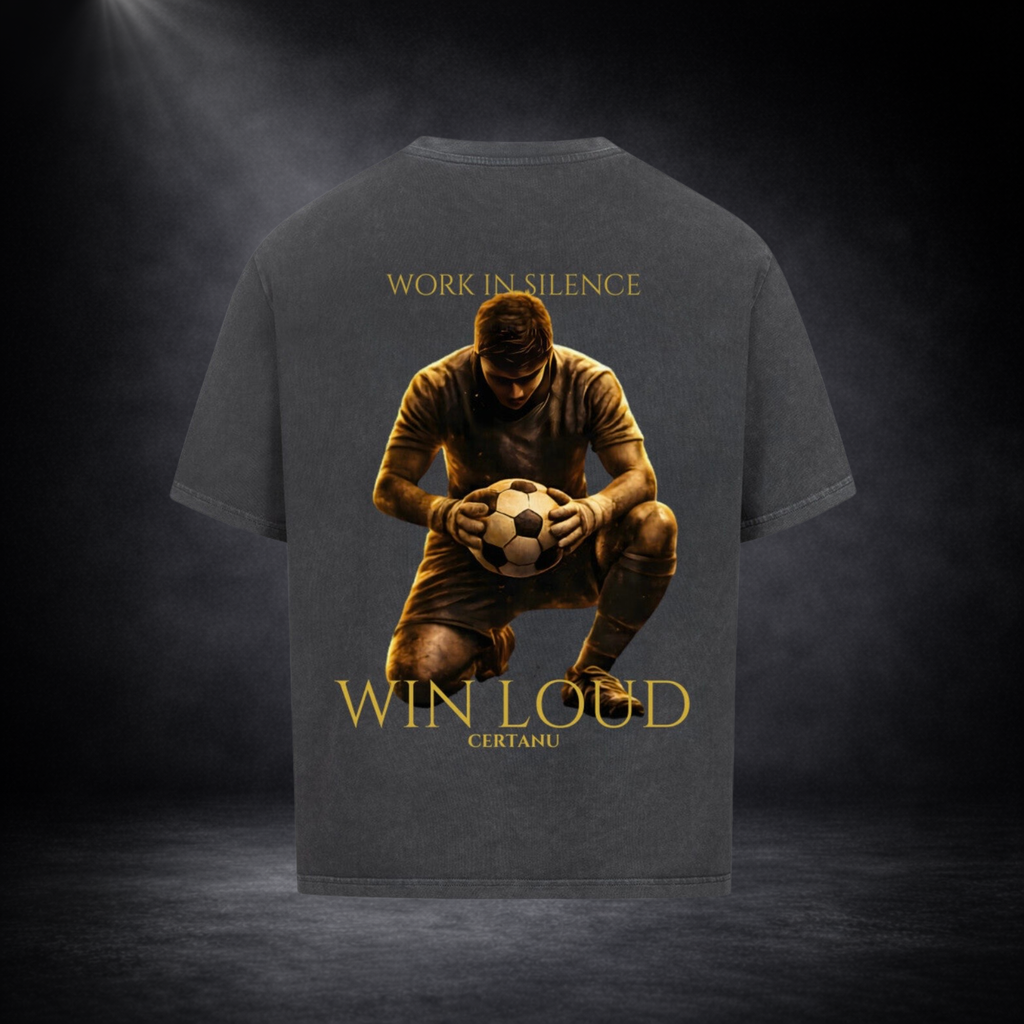 Dunkelgraues oversized T-Shirt in Rückansicht mit großem goldenem Motiv eines knienden Fußballspielers mit Ball, Schriftzug „WORK IN SILENCE“ oben und „WIN LOUD CERTANU“ unten, vor dunklem Studio-Hintergrund