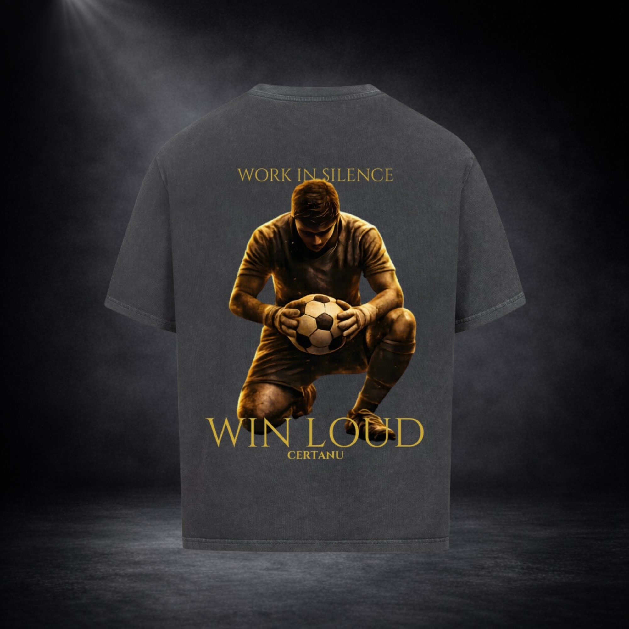 Dunkelgraues oversized T-Shirt in Rückansicht mit großem goldenem Motiv eines knienden Fußballspielers mit Ball, Schriftzug „WORK IN SILENCE“ oben und „WIN LOUD CERTANU“ unten, vor dunklem Studio-Hintergrund