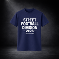 Dunkelblaues T-Shirt mit weißem Aufdruck „STREET FOOTBALL DIVISION 2026 – WORLD GAME“, freigestellt vor dunklem Studio-Hintergrund mit Spotlight, zentrierte Produktansicht