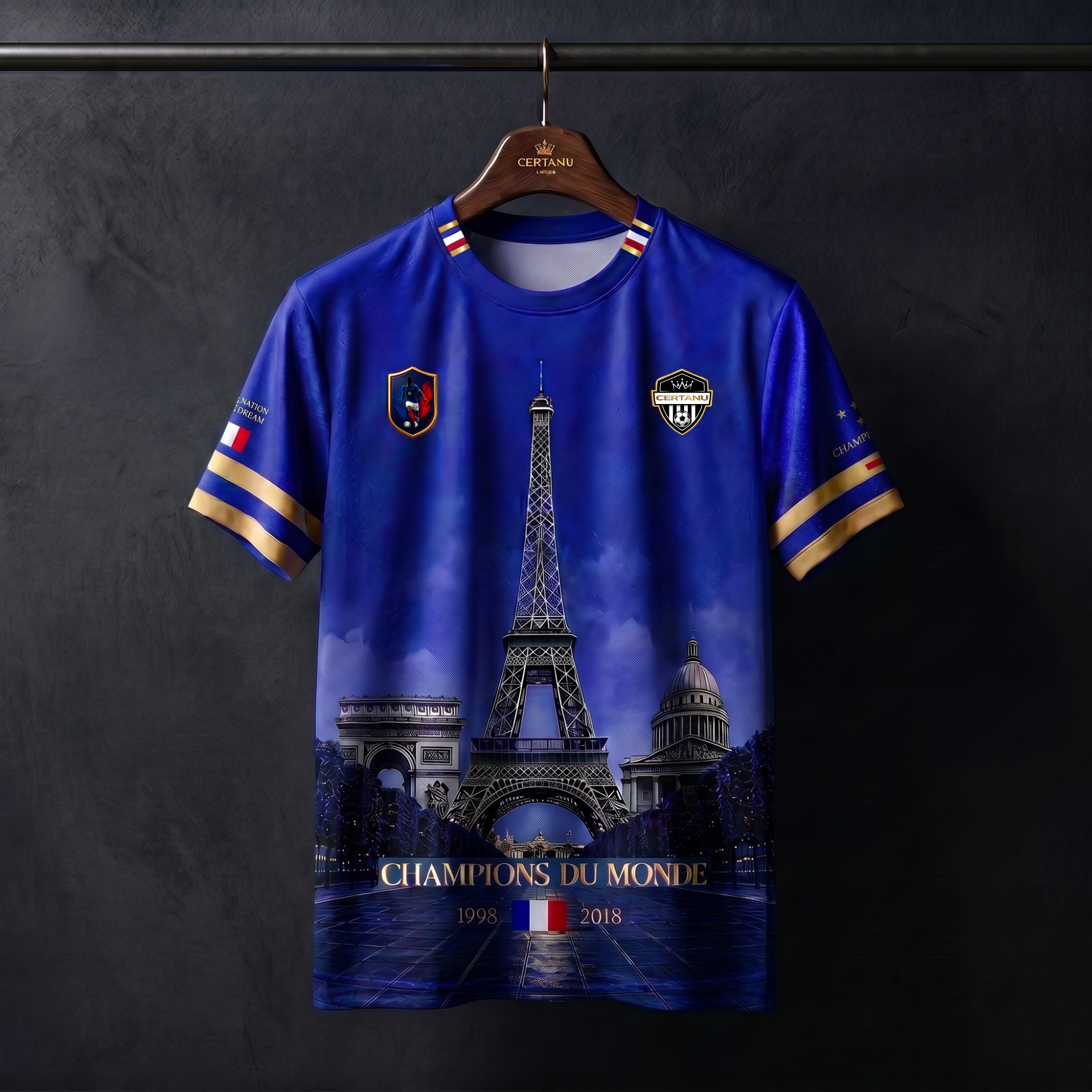 Blaues CERTANU Frankreich Fan-Shirt auf einem dunklen Holzkleiderbügel vor elegantem Studiohintergrund. Das Premium-Design zeigt den Eiffelturm als zentrales Motiv, flankiert vom Arc de Triomphe und dem Panthéon. Im unteren Bereich befindet sich die goldene Aufschrift „Champions du Monde“ mit den Weltmeisterjahren 1998 und 2018 sowie der französischen Flagge. Goldene Ärmelstreifen, französische Trikolore-Details am Kragen und hochwertige CERTANU-Logos unterstreichen den exklusiven Fußball- und Streetwear-St