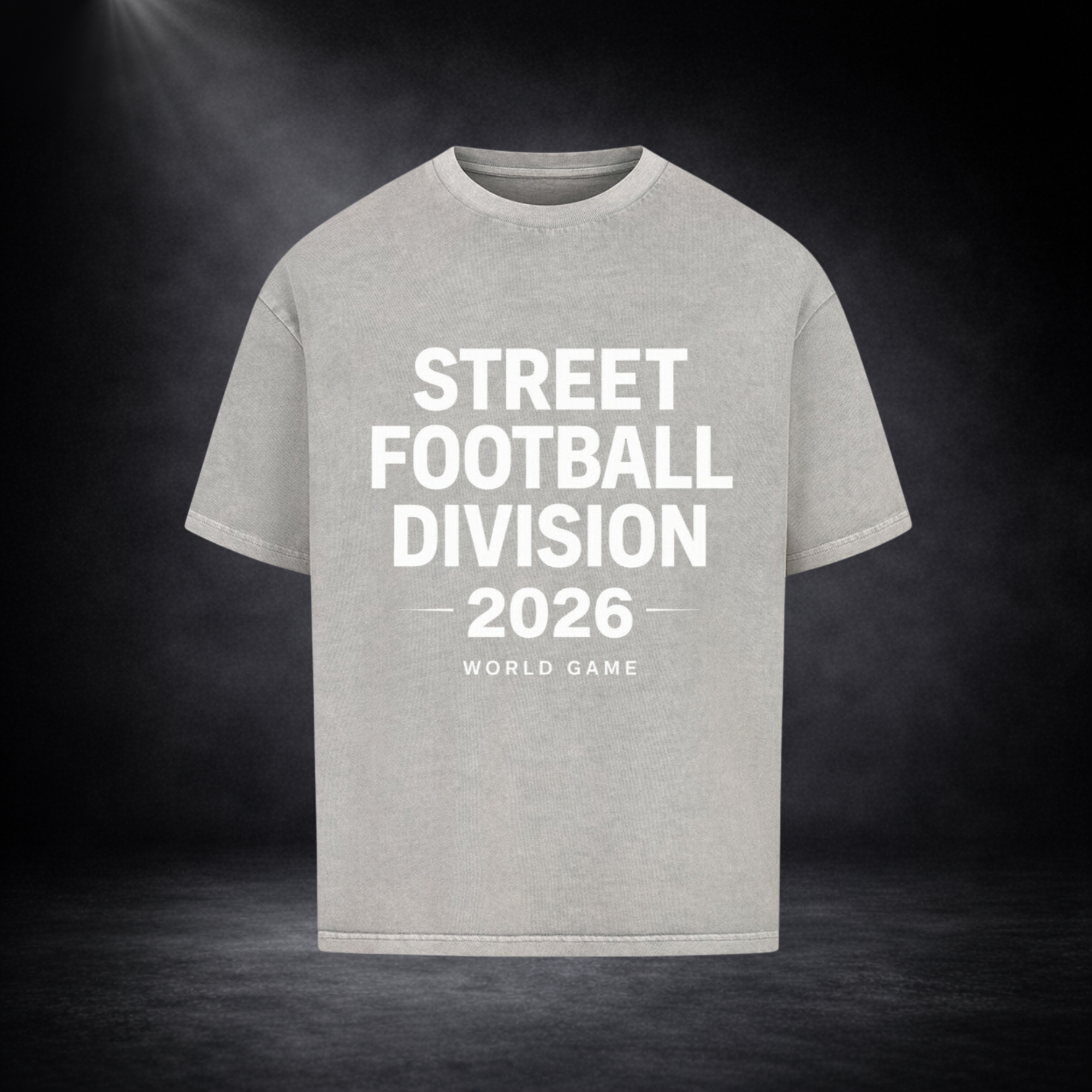 Hellgraues Oversized T-Shirt mit großem weißen Schriftzug „Street Football Division 2026 – World Game“ auf der Vorderseite, vor dunklem Studio-Hintergrund mit Spotlight und leichtem Nebel-Effekt