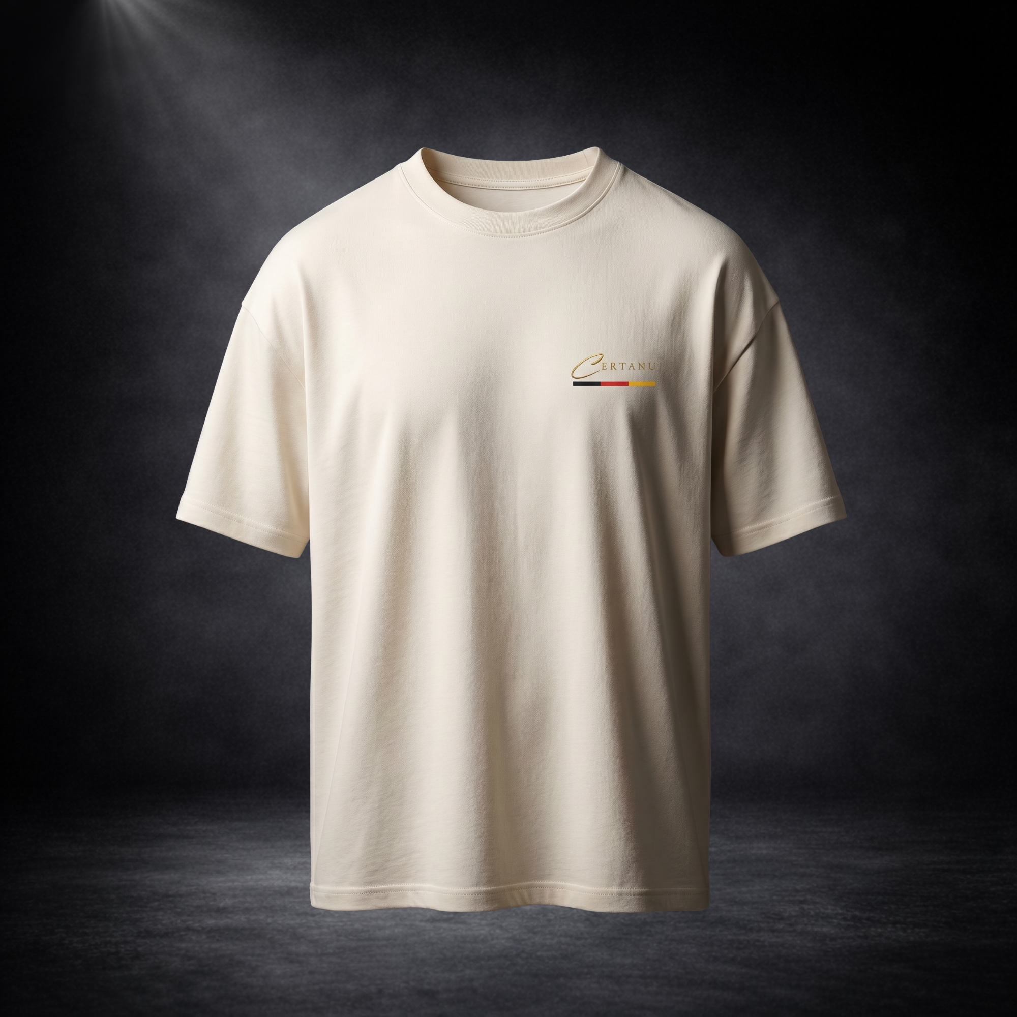 Beiges CERTANU Oversized T-Shirt mit dezentem Brustlogo auf dunklem Studiohintergrund. Das minimalistische Premium-Shirt verfügt über ein elegantes goldenes CERTANU-Logo auf der linken Brust sowie einen schmalen Akzent in den Farben Schwarz, Rot und Gold. Hochwertige Streetwear mit modernem Oversized-Fit, weichem Stoff und zeitlosem Design – ideal für Fußballfans, Freizeit, Alltag und stilvolle Casual-Outfits.