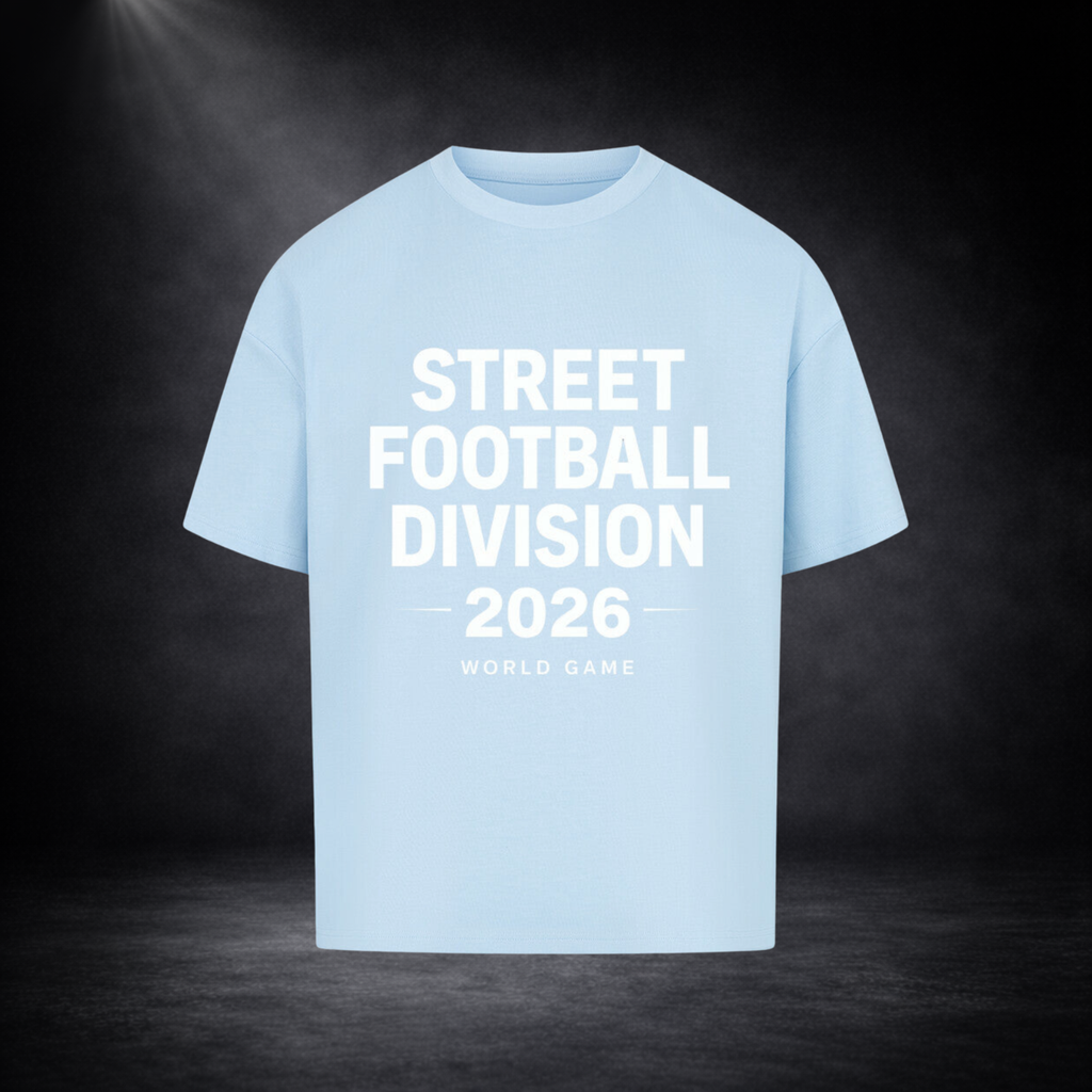 Hellblaues Oversized T-Shirt mit großem weißen Schriftzug „Street Football Division 2026 – World Game“ auf der Vorderseite, dargestellt vor dunklem Studio-Hintergrund mit Spotlight und dezenter Nebelstimmung