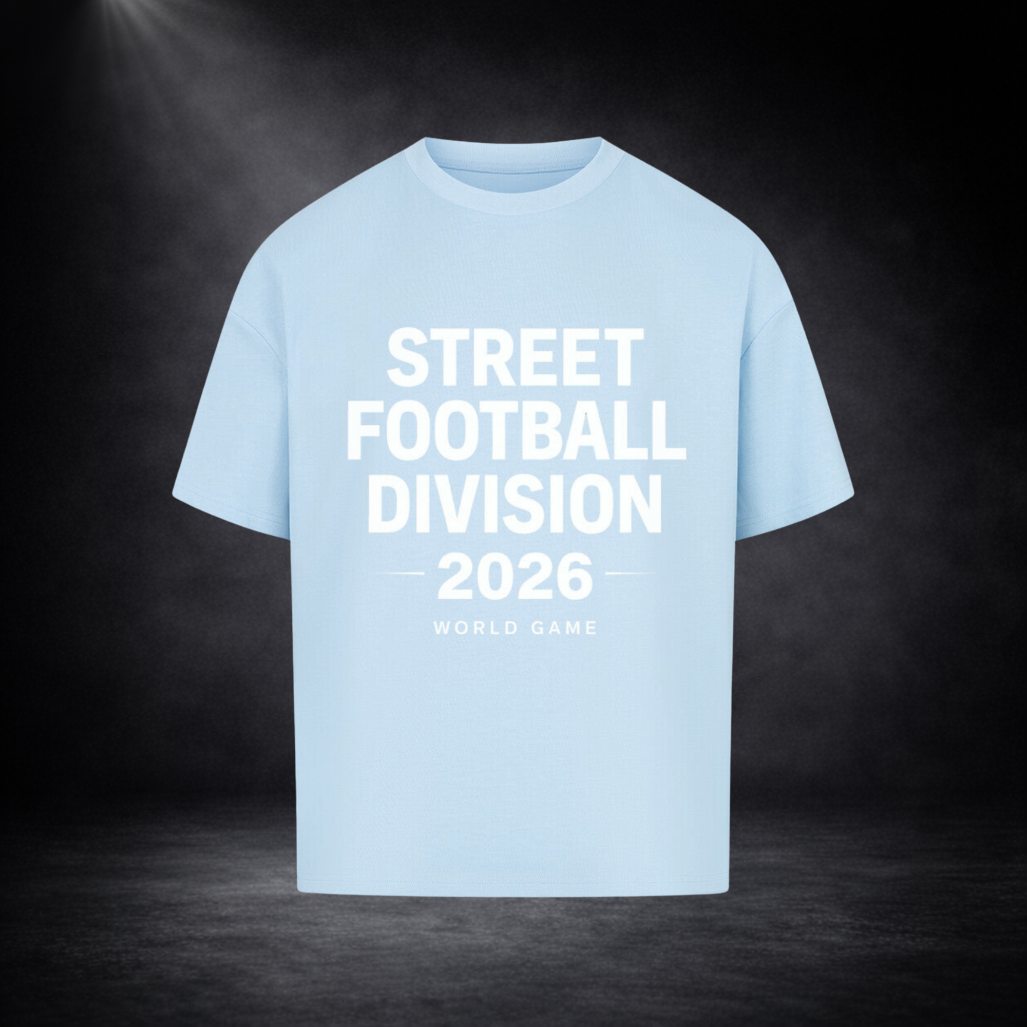 Hellblaues Oversized T-Shirt mit großem weißen Schriftzug „Street Football Division 2026 – World Game“ auf der Vorderseite, dargestellt vor dunklem Studio-Hintergrund mit Spotlight und dezenter Nebelstimmung