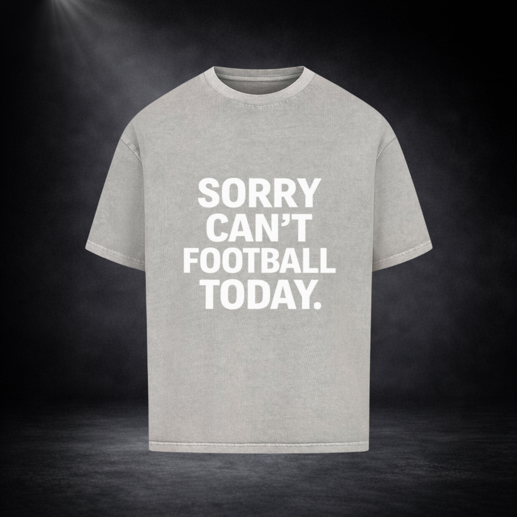 Hellgraues Oversized T-Shirt mit großem weißen Schriftzug „SORRY CAN’T FOOTBALL TODAY.“ auf der Vorderseite, dargestellt vor dunklem Studio-Hintergrund mit sanfter Spotlight-Beleuchtung