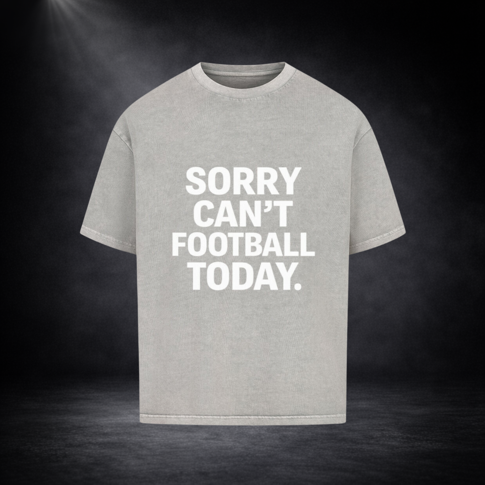 Hellgraues Oversized T-Shirt mit großem weißen Schriftzug „SORRY CAN’T FOOTBALL TODAY.“ auf der Vorderseite, dargestellt vor dunklem Studio-Hintergrund mit sanfter Spotlight-Beleuchtung
