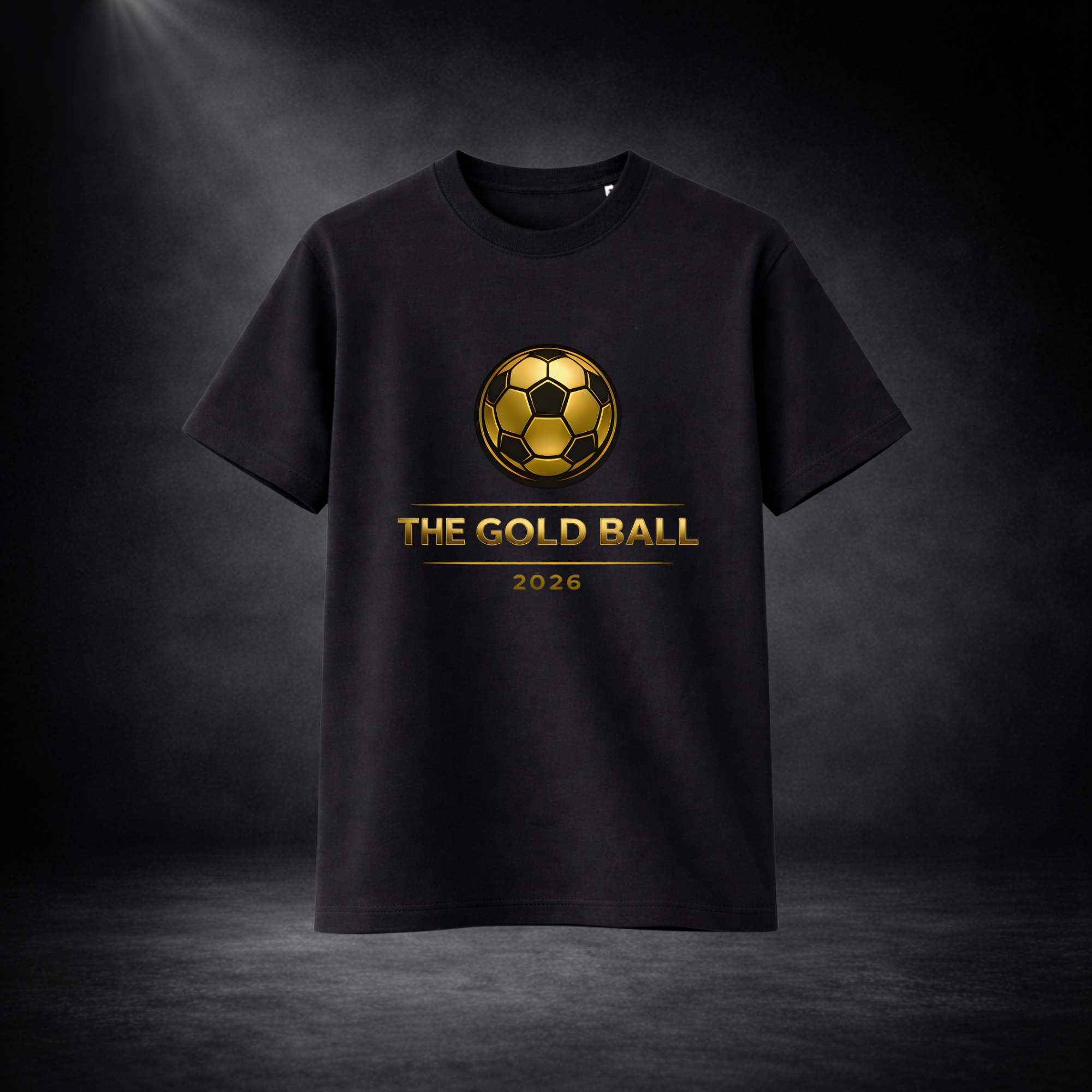Schwarzes T-Shirt mit goldenem Fußball-Logo und dem Schriftzug „THE GOLD BALL 2026“ auf der Vorderseite, freigestellt vor dunklem Studio-Hintergrund mit Spotlight-Effekt