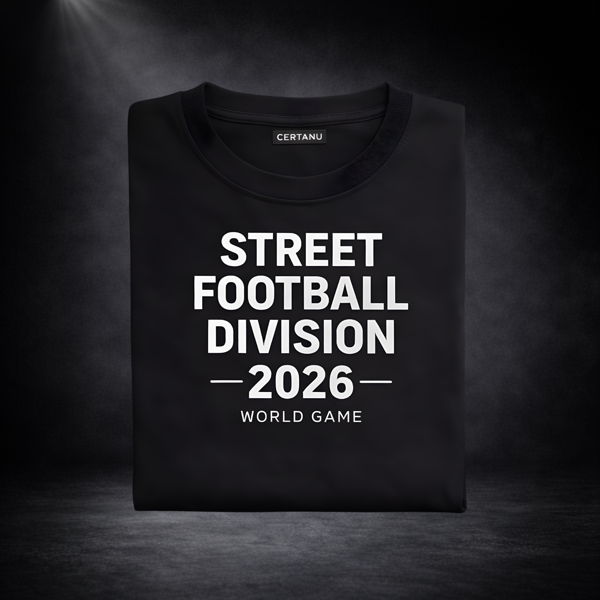 Gefaltetes schwarzes T-Shirt mit weißem Aufdruck „STREET FOOTBALL DIVISION 2026 – WORLD GAME“ und sichtbarem CERTANU-Label, vor dunklem Studio-Hintergrund mit Spotlight