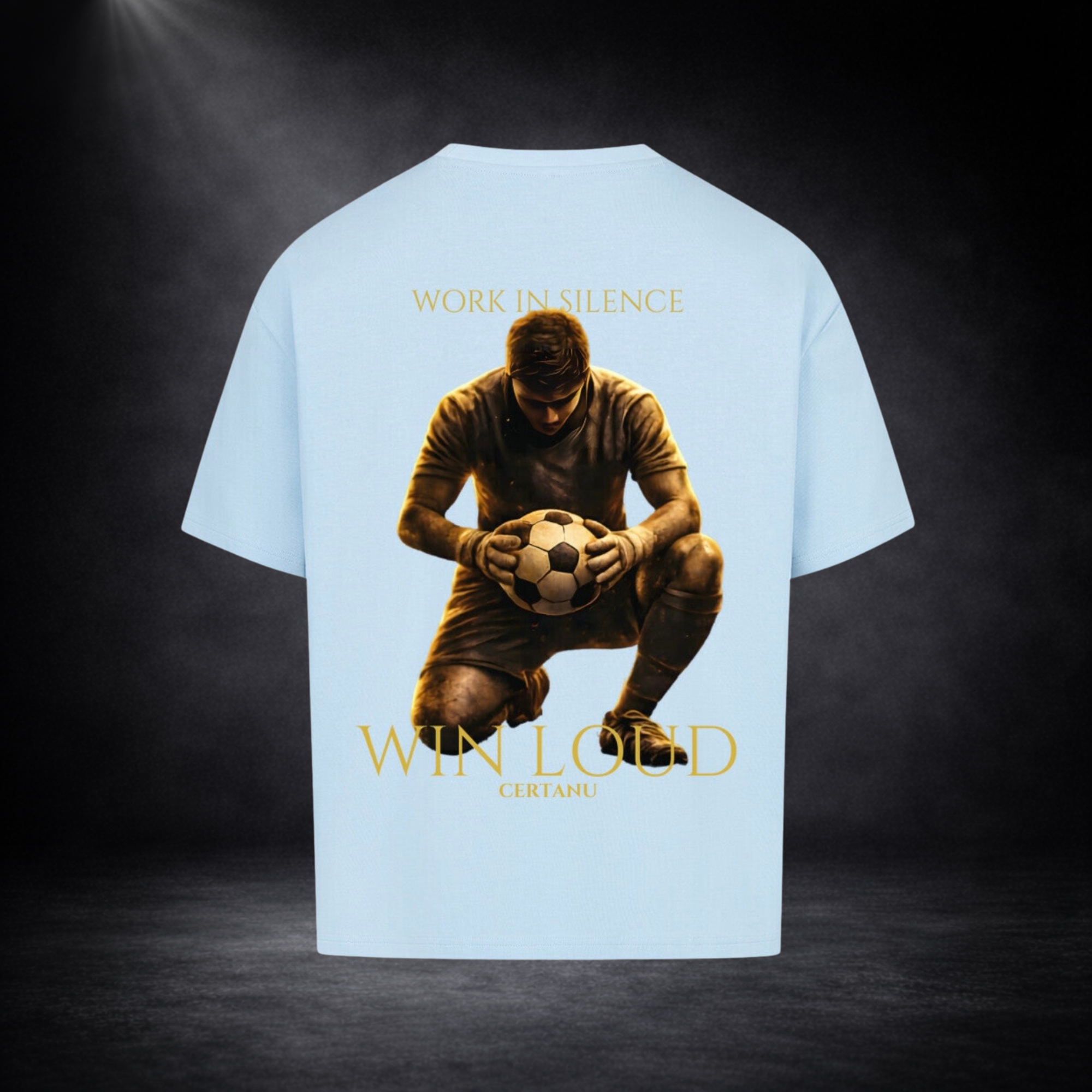 Hellblaues oversized T-Shirt in Rückansicht mit großem goldenem Motiv eines knienden Fußballspielers mit Ball, Schriftzug „WORK IN SILENCE“ oben und „WIN LOUD CERTANU“ unten, vor dunklem Studio-Hintergrund