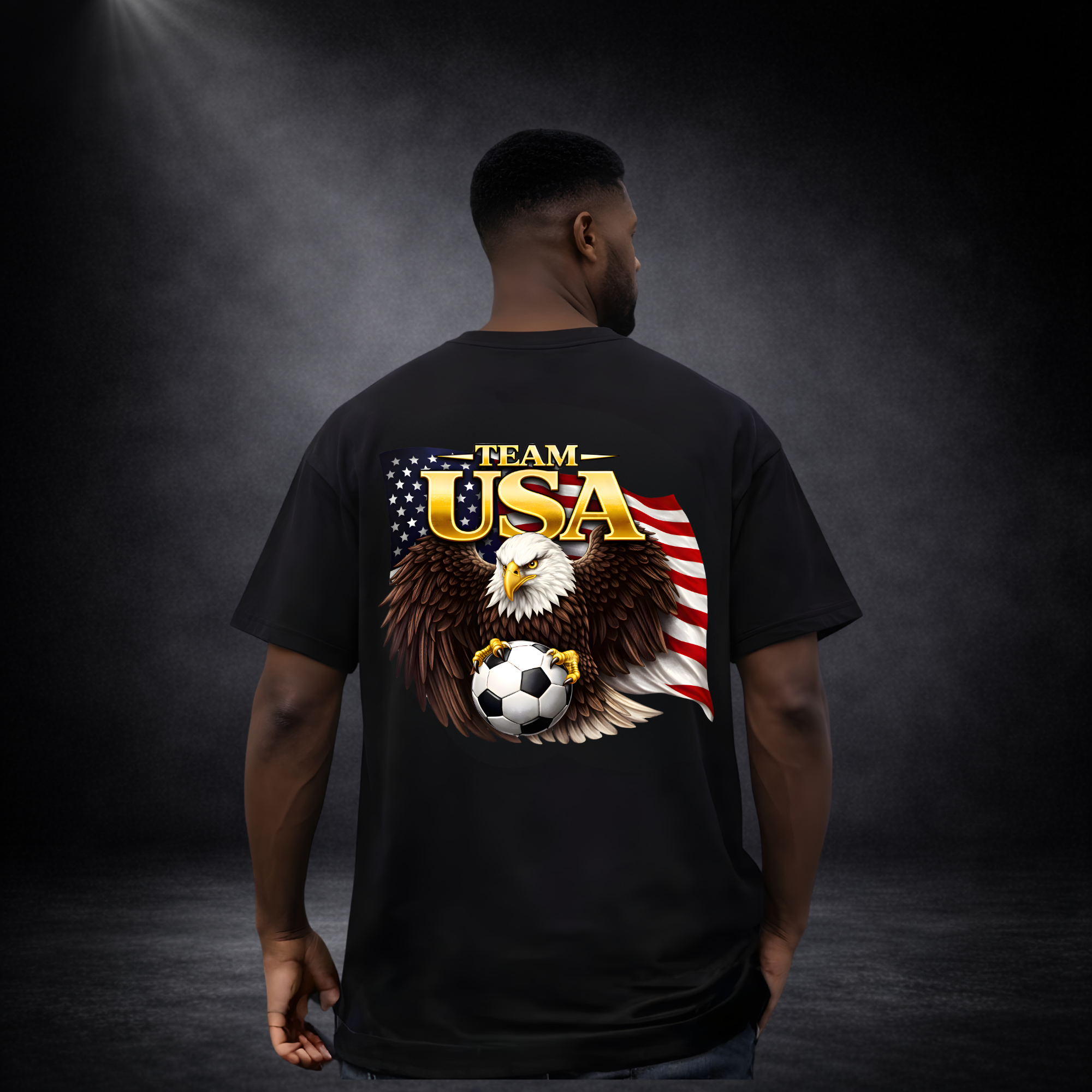 Rückansicht eines Mannes in schwarzem oversized T-Shirt mit großem „Team USA“-Design, Adler mit Fußball vor US-Flagge auf dunklem Studio-Hintergrund
