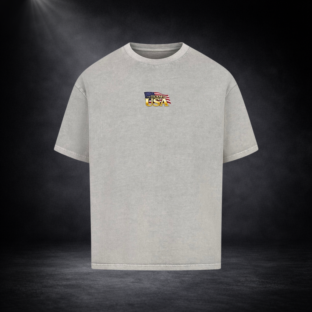 Graue oversized T-Shirt Vorderseite mit kleinem „Team USA“-Logo auf der Brust, US-Flaggen-Element, dunkler Studio-Hintergrund