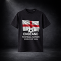 Schwarzes T-Shirt mit England-Flagge und Fußballmotiv, darunter Schriftzug „England Football Nation World Cup 2026“, präsentiert vor dunklem Studio-Hintergrund