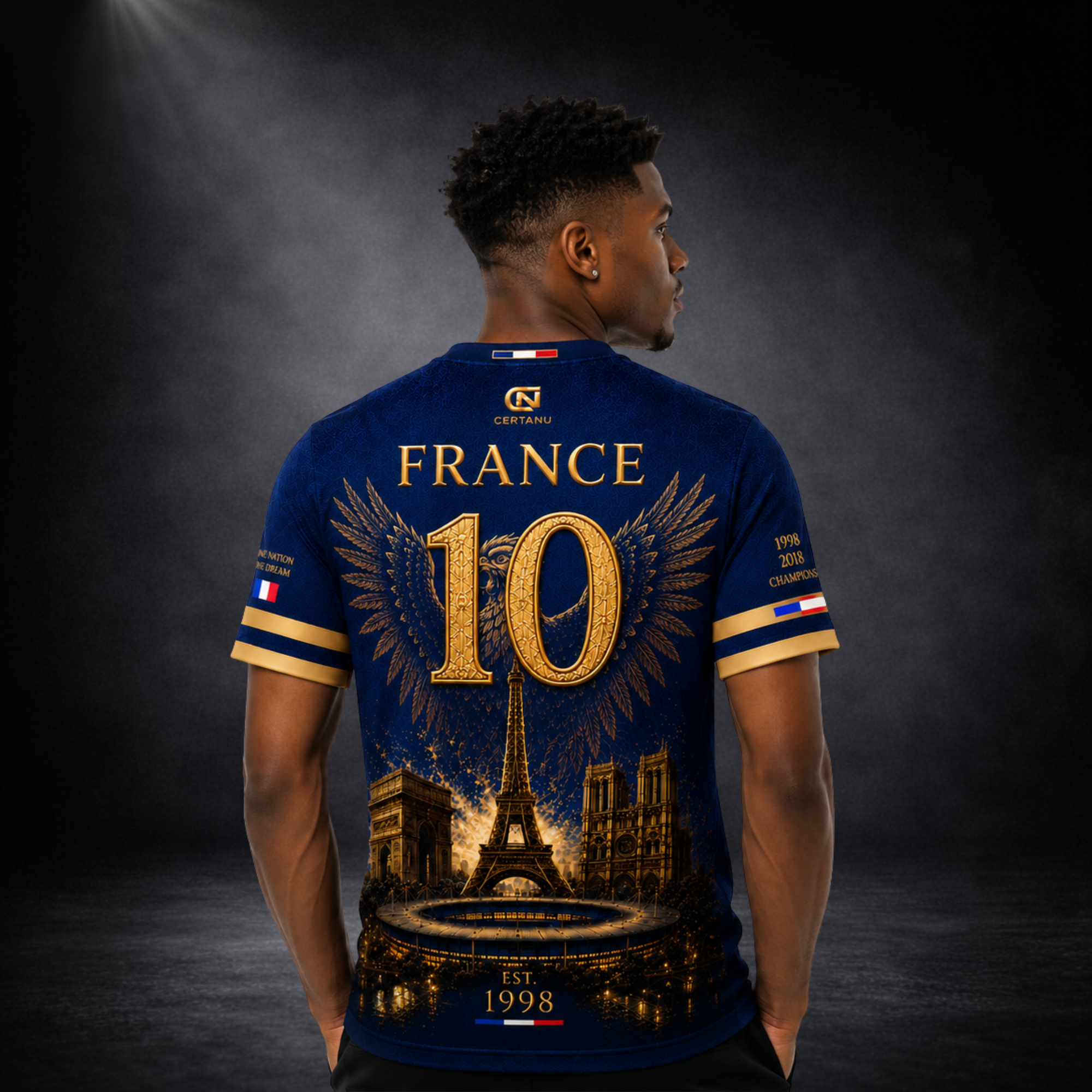 Rückansicht eines männlichen Models mit dunkelblauem CERTANU Frankreich Fan-Shirt im Premium-Football-Streetwear-Stil. Das Rückendesign zeigt die große goldene Nummer 10 mit ausgebreiteten Flügeln, den Schriftzug „FRANCE“, den Eiffelturm, den Arc de Triomphe, die Kathedrale Notre-Dame und ein beleuchtetes Stadion. Goldene Details sowie die Jahreszahlen 1998 und 2018 erinnern an die Weltmeistertitel Frankreichs. Exklusives Fußball-Fanshirt mit französischen Flaggen-Elementen, ideal für WM, EM, Stadionbesuche