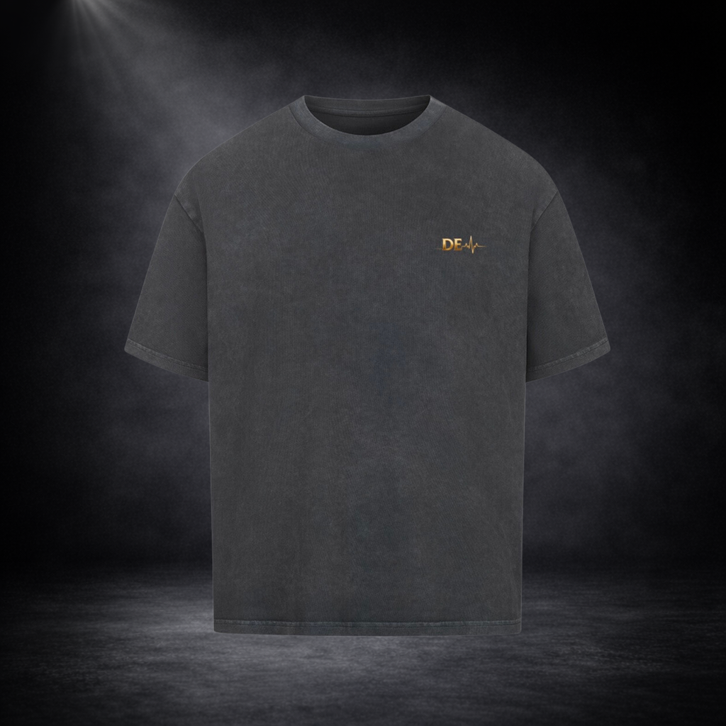 Dunkelgraues T-Shirt in Frontansicht vor dunklem Studio-Hintergrund, mit kleinem goldenen „DE“-Logo und Herzschlag-Linie auf der Brust in dezentem Design