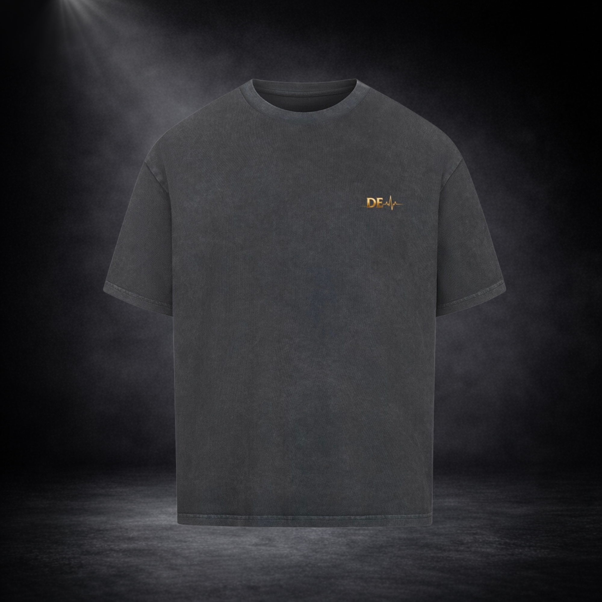 Dunkelgraues T-Shirt in Frontansicht vor dunklem Studio-Hintergrund, mit kleinem goldenen „DE“-Logo und Herzschlag-Linie auf der Brust in dezentem Design