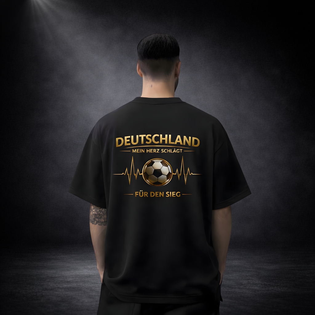 Mann von hinten vor dunklem Studio-Hintergrund, trägt ein schwarzes Oversize-T-Shirt mit großem goldenem Fußball-Design und Schriftzug „Deutschland – Mein Herz schlägt für den Sieg“ im Premium-Stil