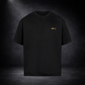Schwarzes T-Shirt vor dunklem Studio-Hintergrund, minimalistisch präsentiert mit kleinem goldenen Brustlogo, cleanes und hochwertiges Design