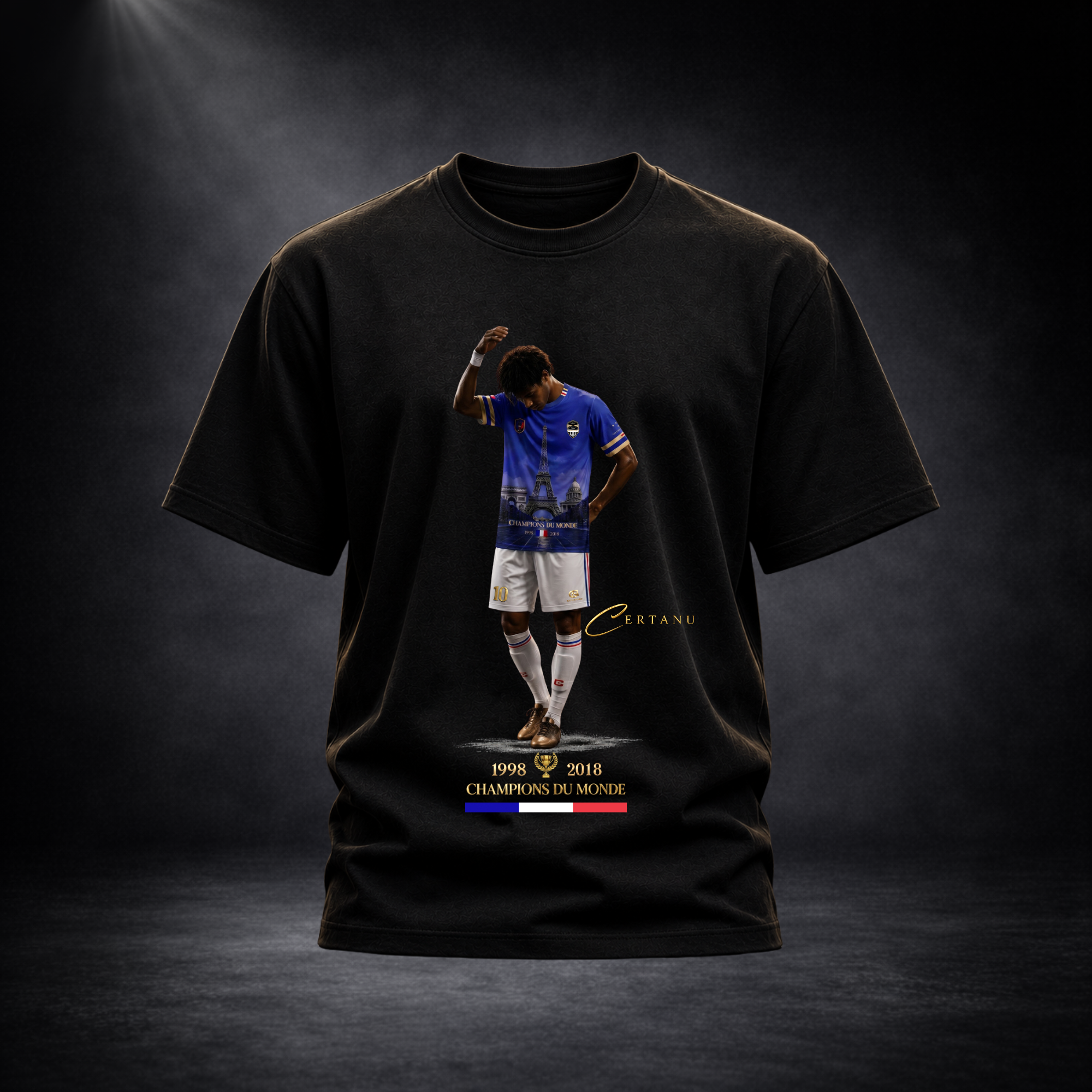 Produktaufnahme eines schwarzen CERTANU Premium T-Shirts vor dunklem Studiohintergrund mit edler Spotlight-Beleuchtung. Auf der Vorderseite befindet sich ein exklusives Frankreich-Fußballmotiv mit einem Spieler im blauen Trikot, integriertem Eiffelturm-Design und goldenen CERTANU-Details. Unter dem Motiv stehen die Weltmeisterjahre 1998 und 2018 sowie der Schriftzug „Champions du Monde“ mit französischer Trikolore in Blau, Weiß und Rot. Das hochwertige Fan-Shirt verbindet moderne Streetwear mit französische