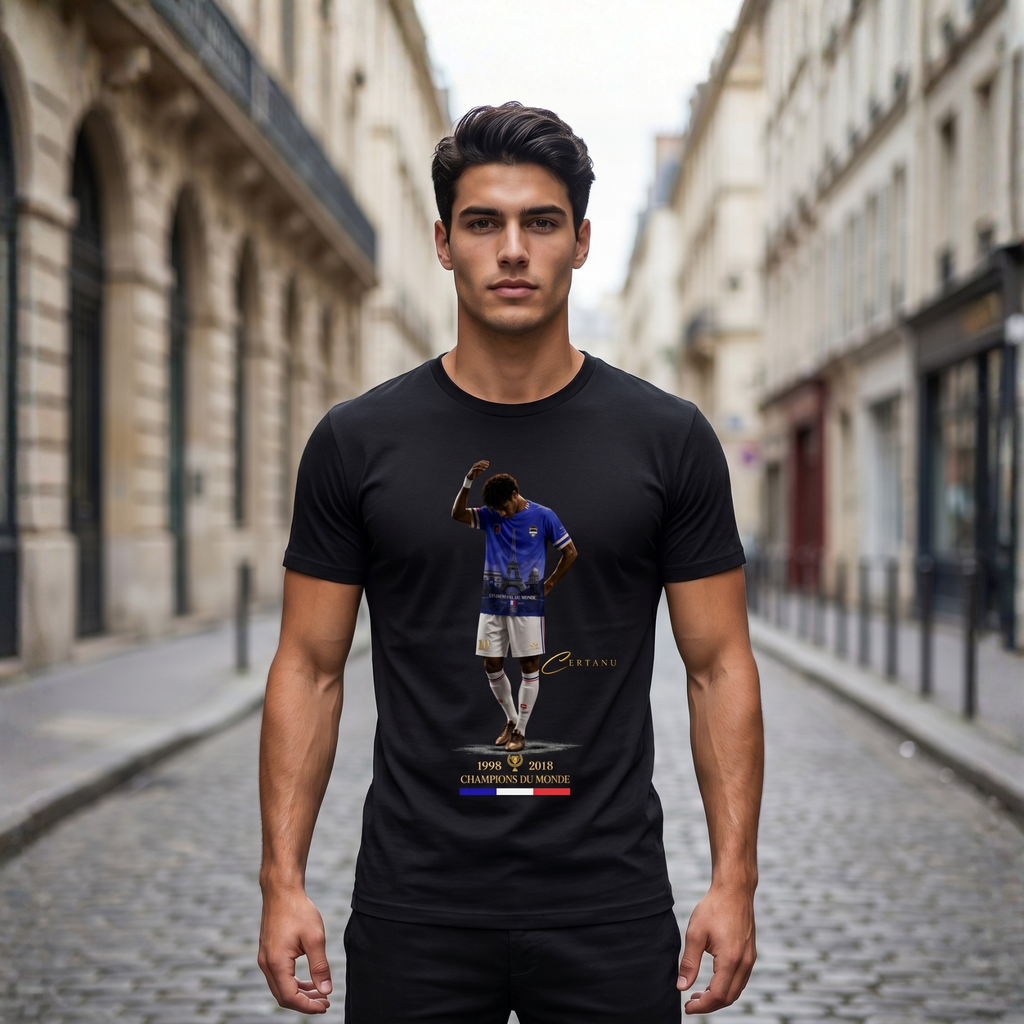 Junger Mann trägt ein schwarzes CERTANU Premium T-Shirt in einer eleganten Pariser Altstadtstraße mit klassischer französischer Architektur im Hintergrund. Das Frontdesign zeigt einen Fußballspieler im blauen Frankreich-Trikot mit integriertem Eiffelturm-Motiv, goldenen CERTANU-Details sowie den Weltmeisterjahren 1998 und 2018. Unter dem Motiv befindet sich der Schriftzug „Champions du Monde“ mit französischer Trikolore in Blau, Weiß und Rot. Das Lifestyle-Foto verbindet moderne Streetwear mit französischer